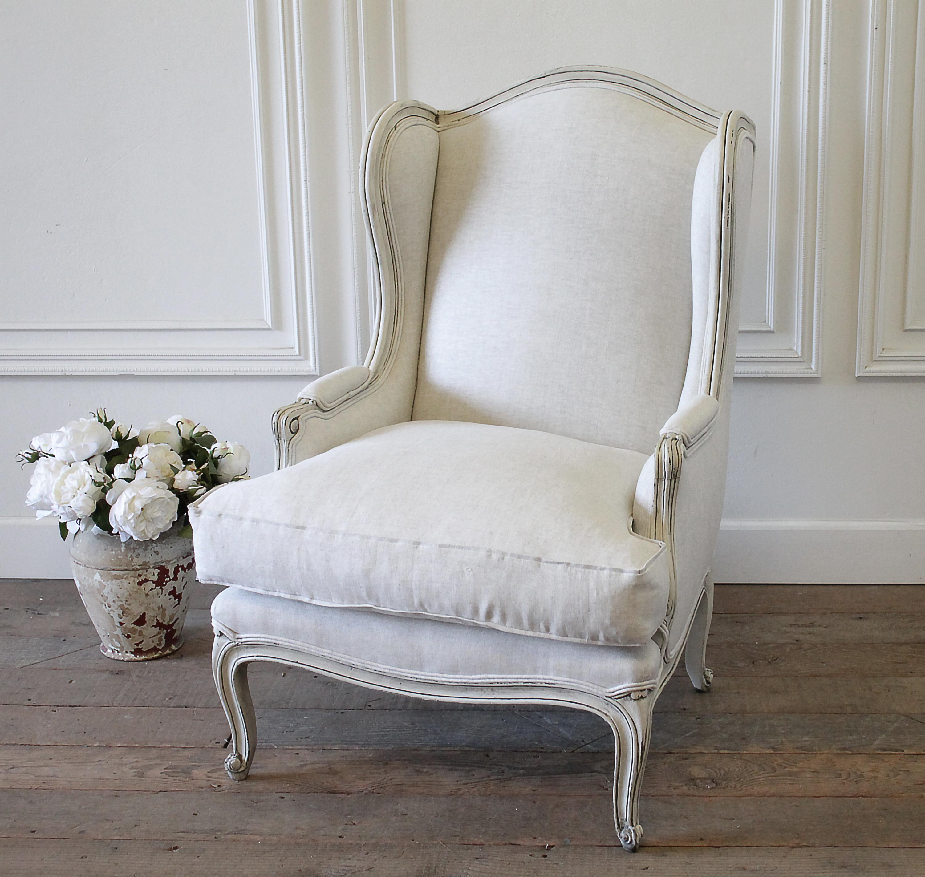 Vintage French Provincial wingback style chair upholstered in natural linen painted in our oyster white, which is an off white with subtle distressed edges, and antique glazed patina. Legs are solid and sturdy, cushion is down wrapped, medium-firm