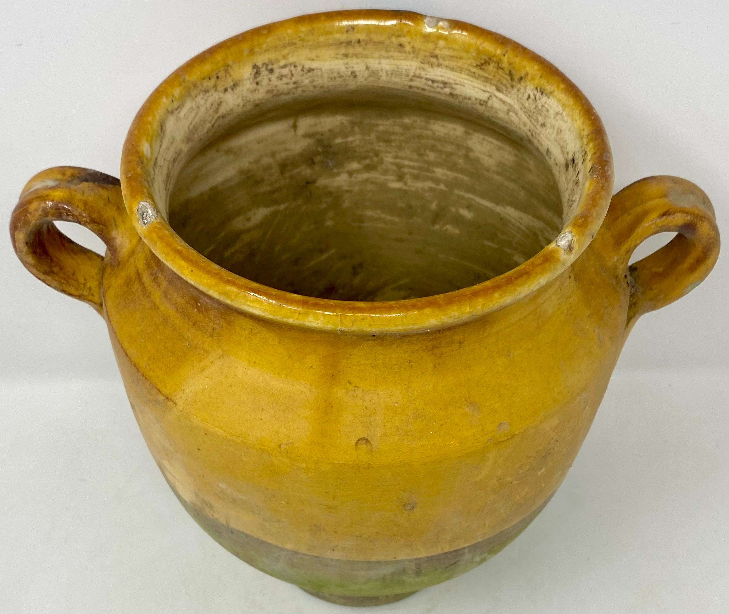 Vieux pot à confit de fabrication artisanale de style provincial français, en terre cuite émaillée jaune, avec poignées.
Sur la dernière photo, nous en avons quelques-uns de différentes tailles et formes. Chacun d'entre eux présente une usure
