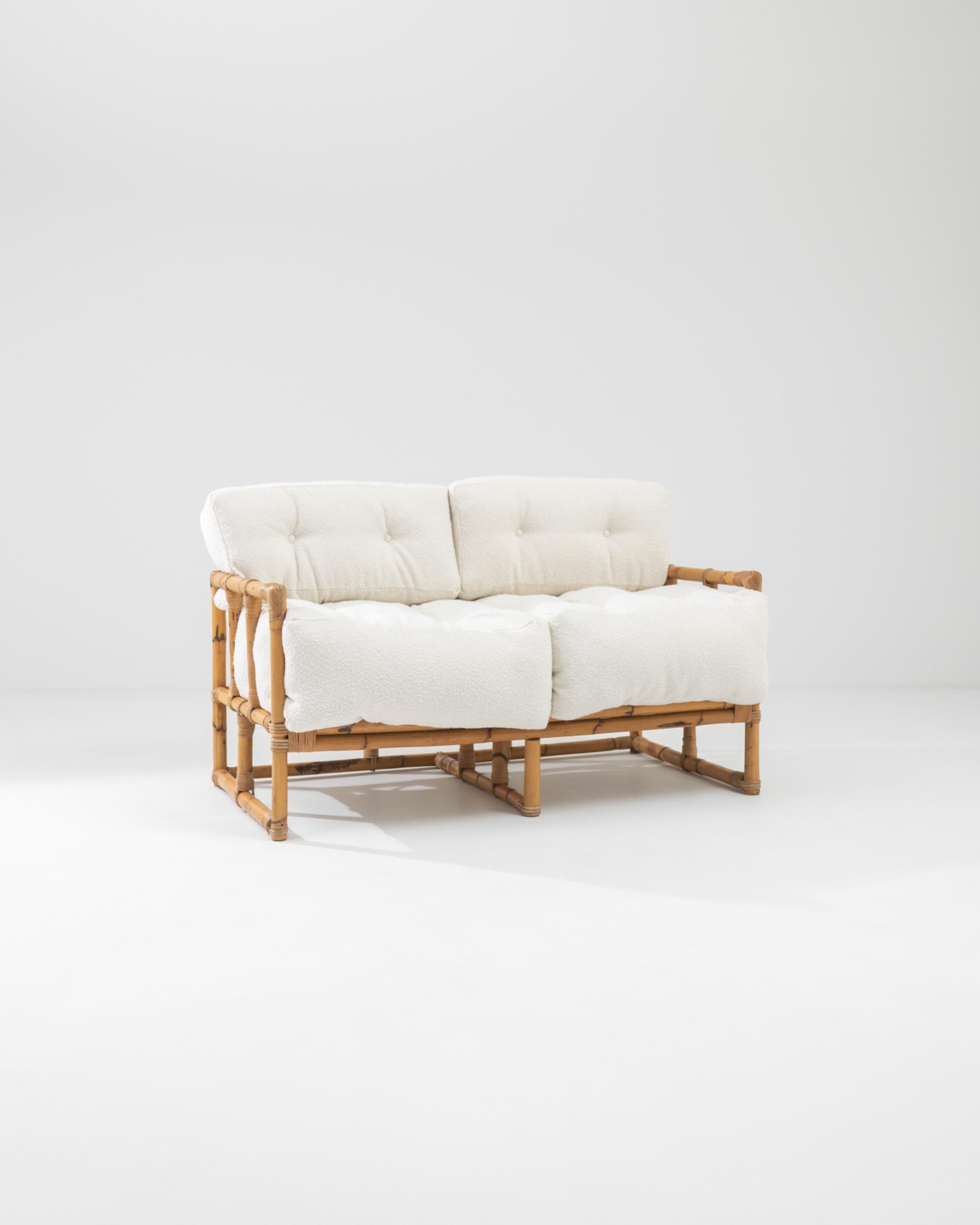 A rattan upholstered sofa made in 20th century France. A creamy off-white boucle upholstery provides vivacious new life to this retro treasure. Paired with an updated fabric, the natural material emits an aura of calm, the pleasing synergy inviting