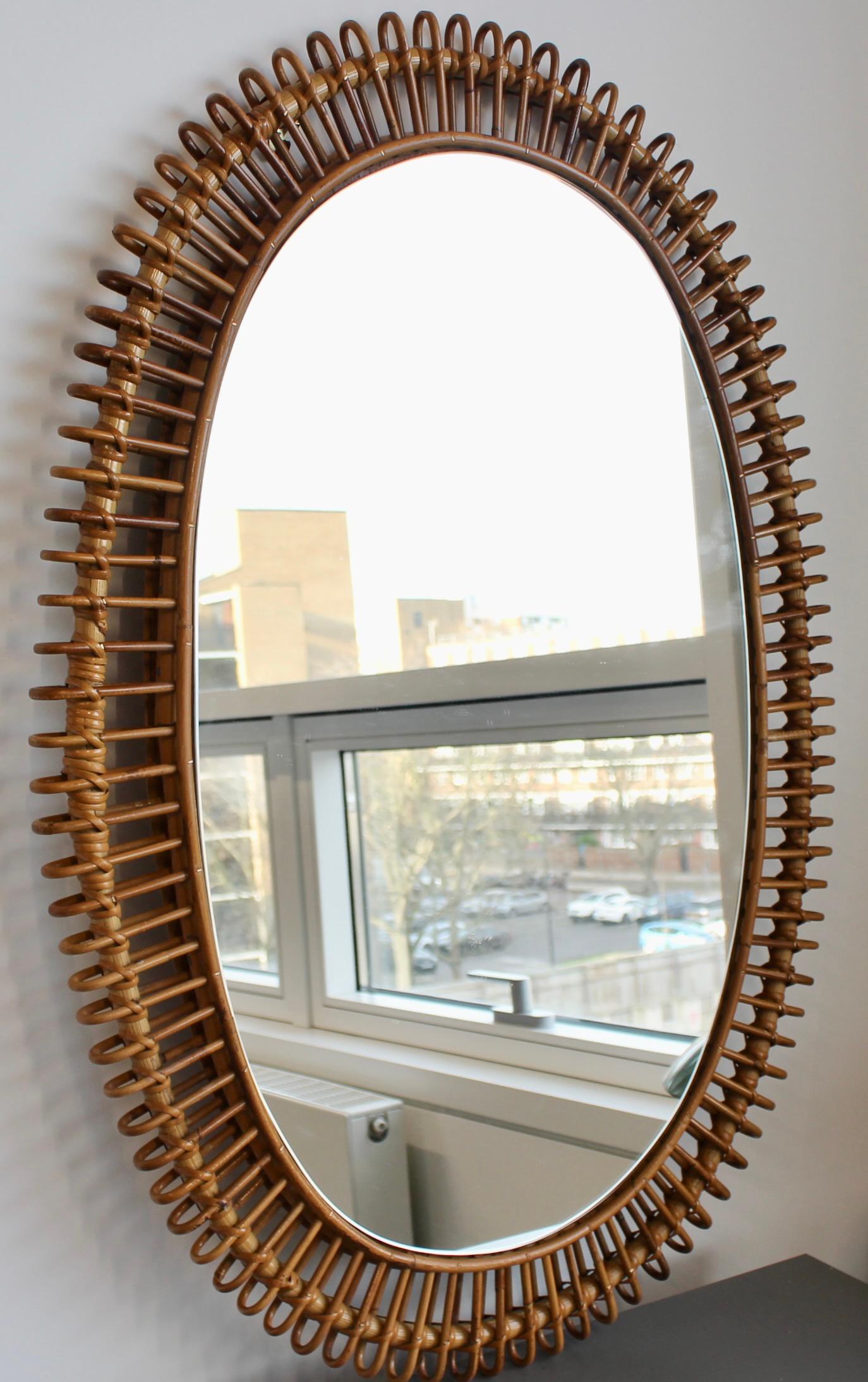 French rattan oval-shaped wall mirror (circa 1960s). A distinctive vintage mirror which transports you immediately to another place and another time, perhaps the French Riviera or Miami's South Beach circa 1960. Its elegant glass is oval-shaped,