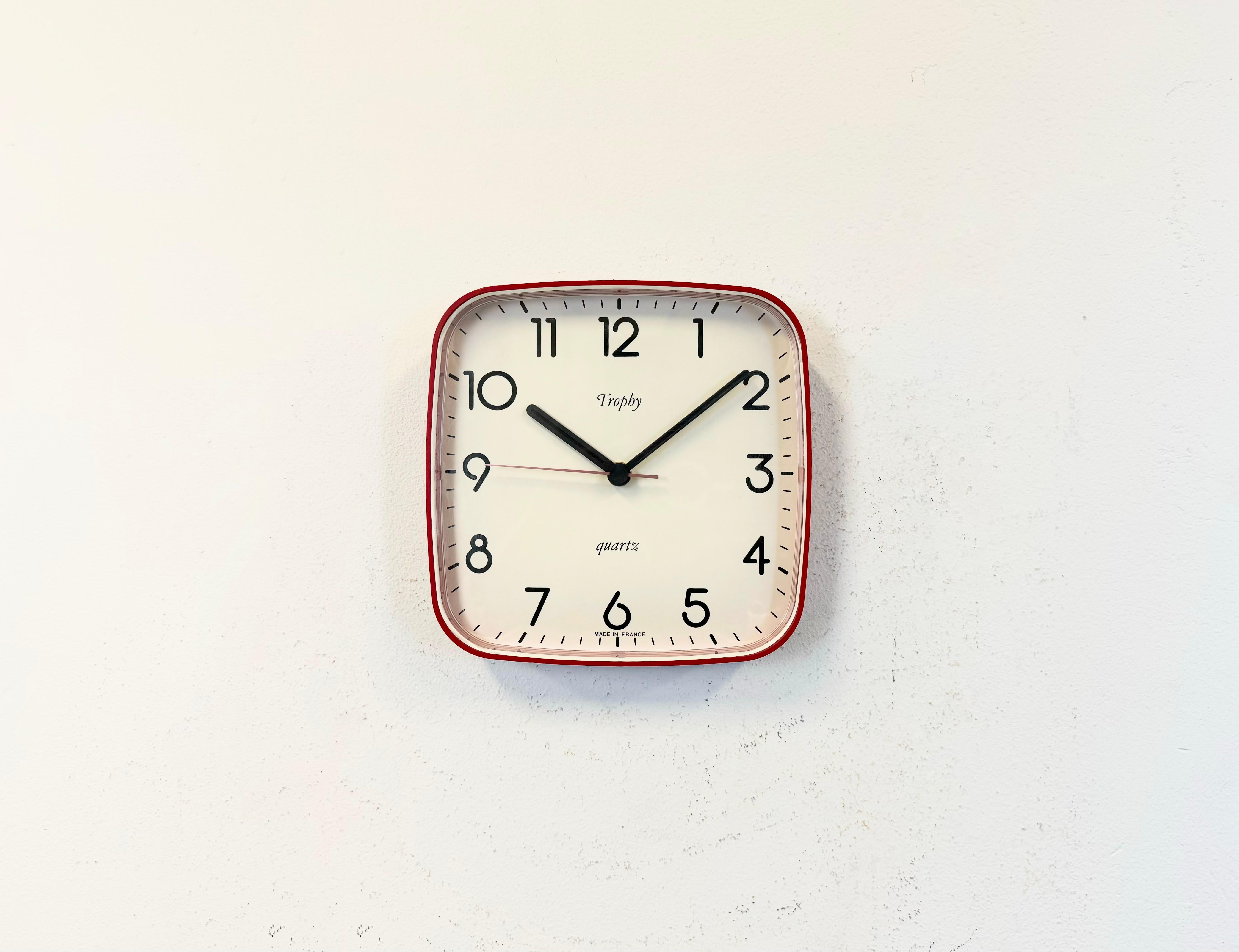 Cette horloge murale vintage en bakélite a été fabriquée par Trophy en France dans les années 1990. Il se caractérise par un corps en bakélite rouge et un couvercle en plastique transparent. Le mécanisme d'origine fonctionne parfaitement et
