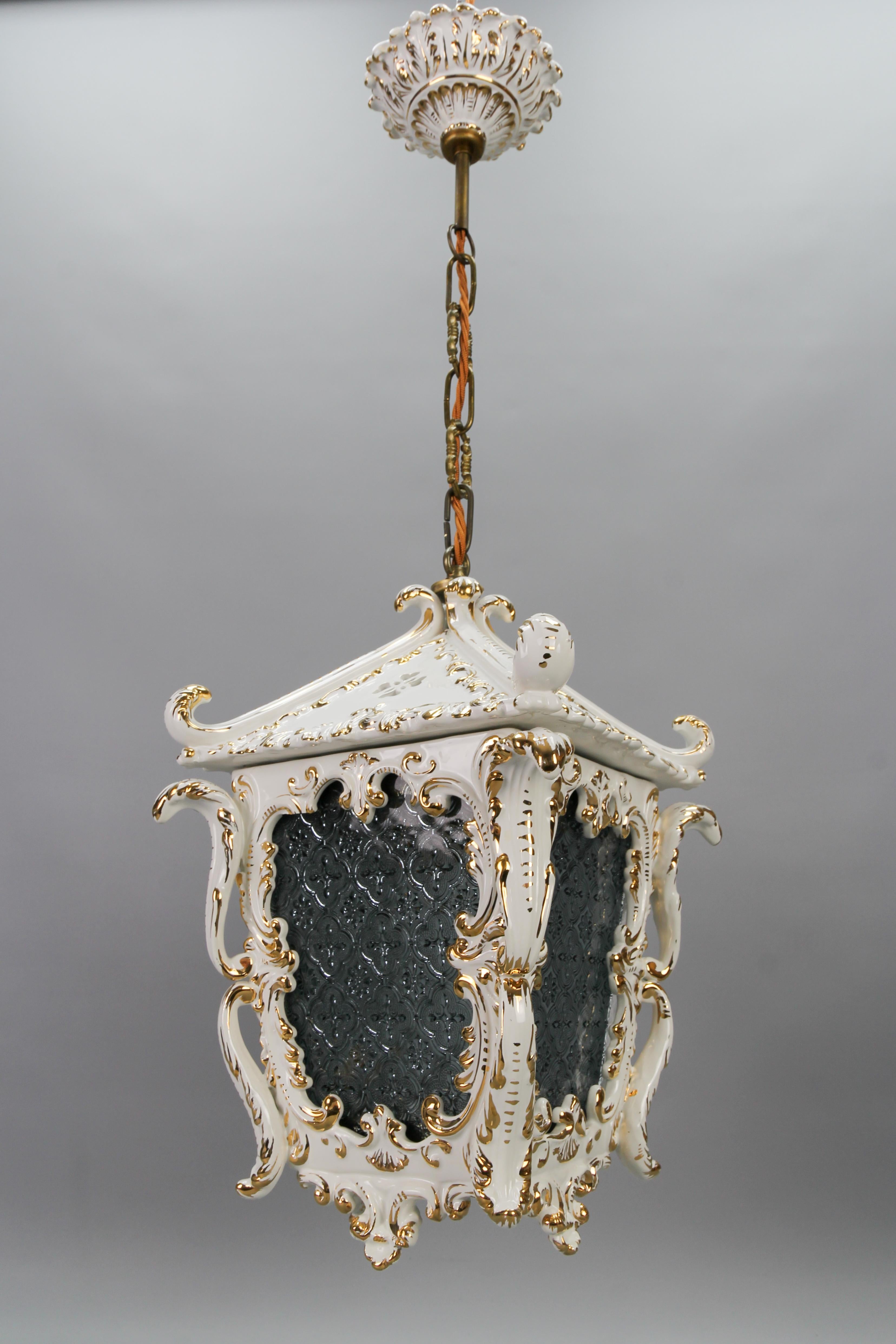 Vintage Rococo style white ceramic and glass hanging lantern, France, circa the 1970s.
This adorable pendant light fixture features a white ceramic lantern and a beautiful canopy with golden accents - Rococo-style scrolls, and leaves. Four ornate