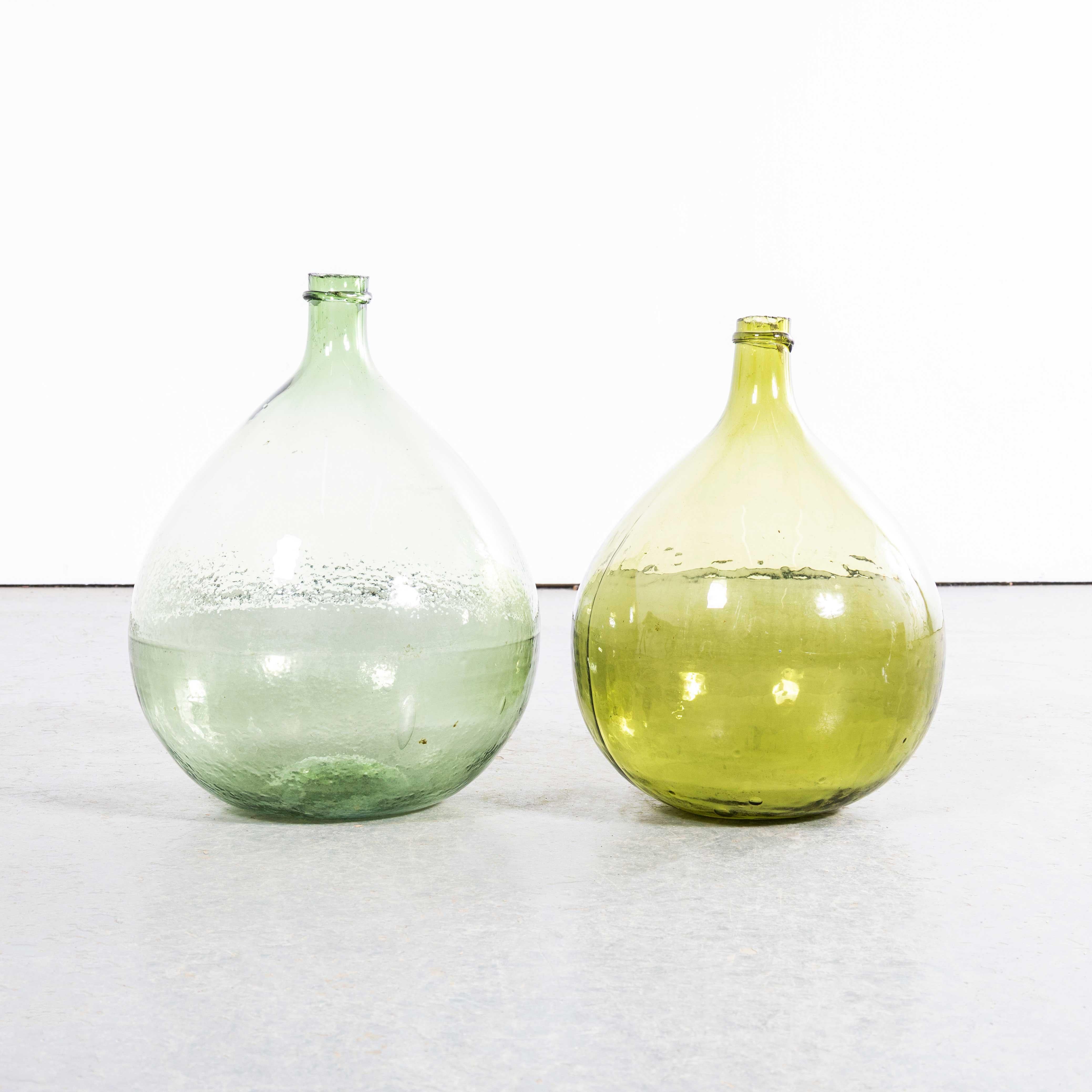 Damigiane rotonde francesi d'epoca in vetro verde e ambra - Coppia. 

Una coppia di damigiane in vetro soffiato a bocca utilizzate come contenitori tradizionali principalmente per la conservazione e il trasporto del vino. Queste damigiane sono state
