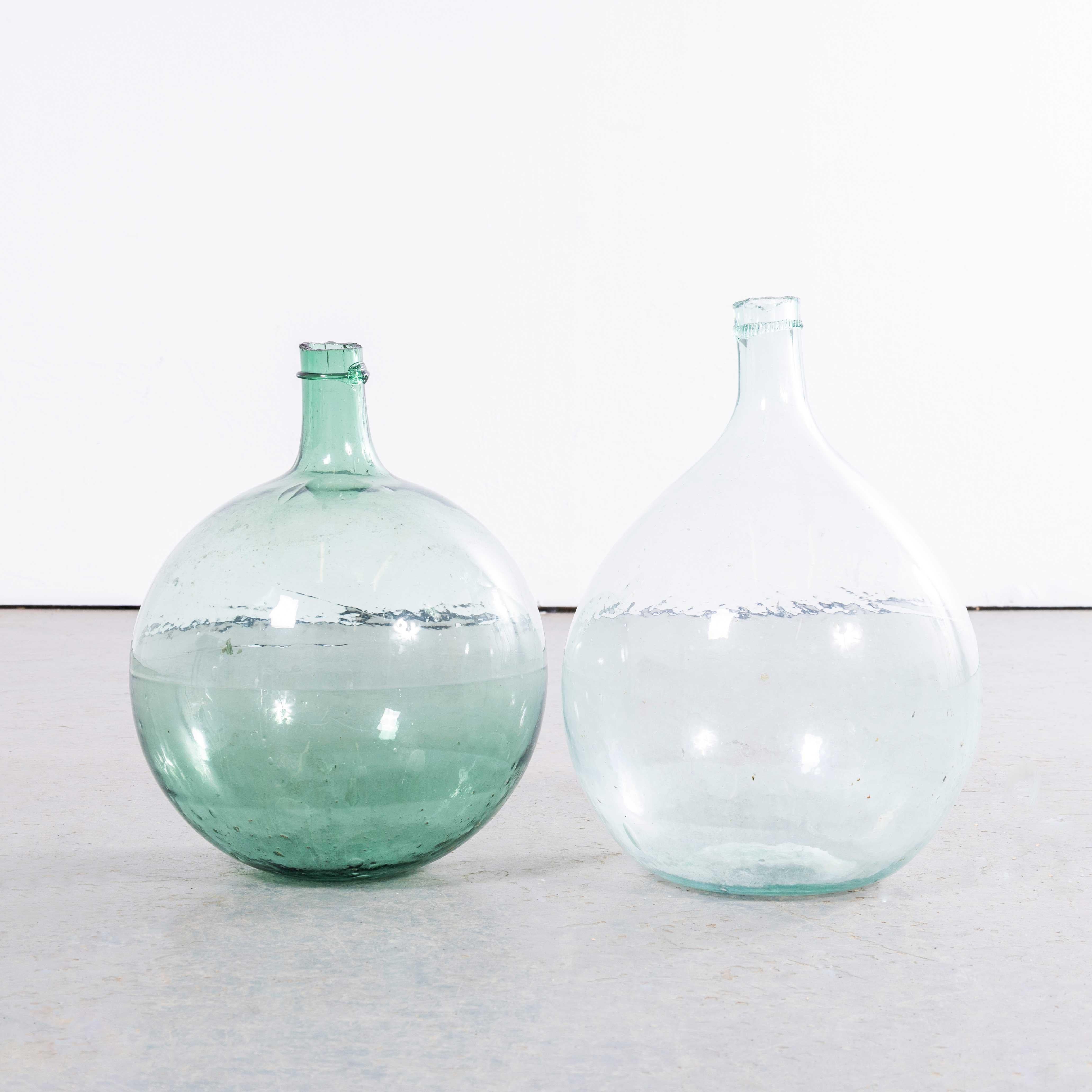 Damigiane rotonde francesi d'epoca in vetro Greene & Greene Light - Coppia. Una coppia di damigiane in vetro soffiato a bocca utilizzate come contenitori tradizionali principalmente per la conservazione e il trasporto del vino. Queste damigiane sono