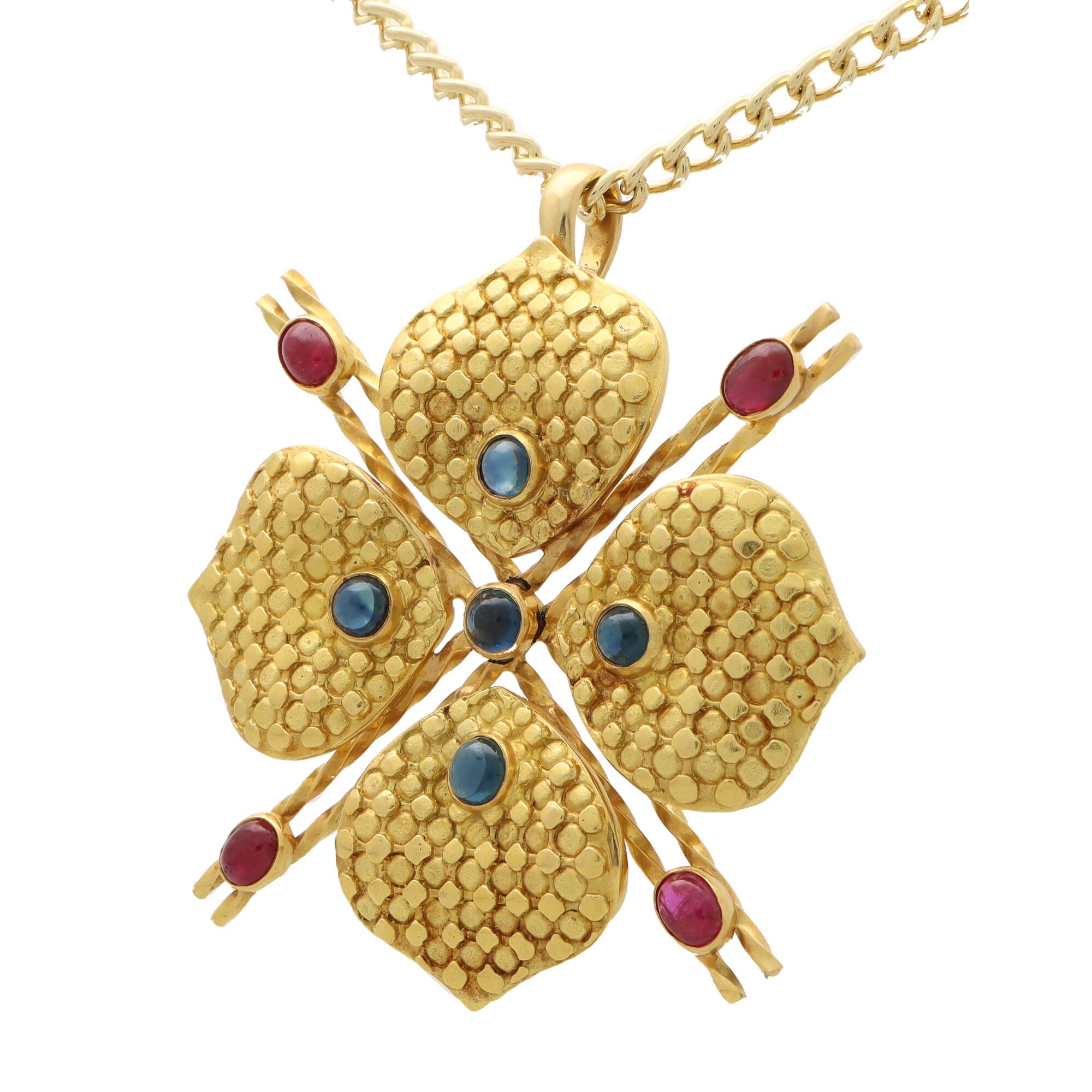 A beautiful vintage French ruby and sapphire clover pendant set in 18k yellow gold.

The pendant is designed as a clover on top of an openwork double X motif. Each of the four clover leaves is bezel set with a circular cabochon sapphire and