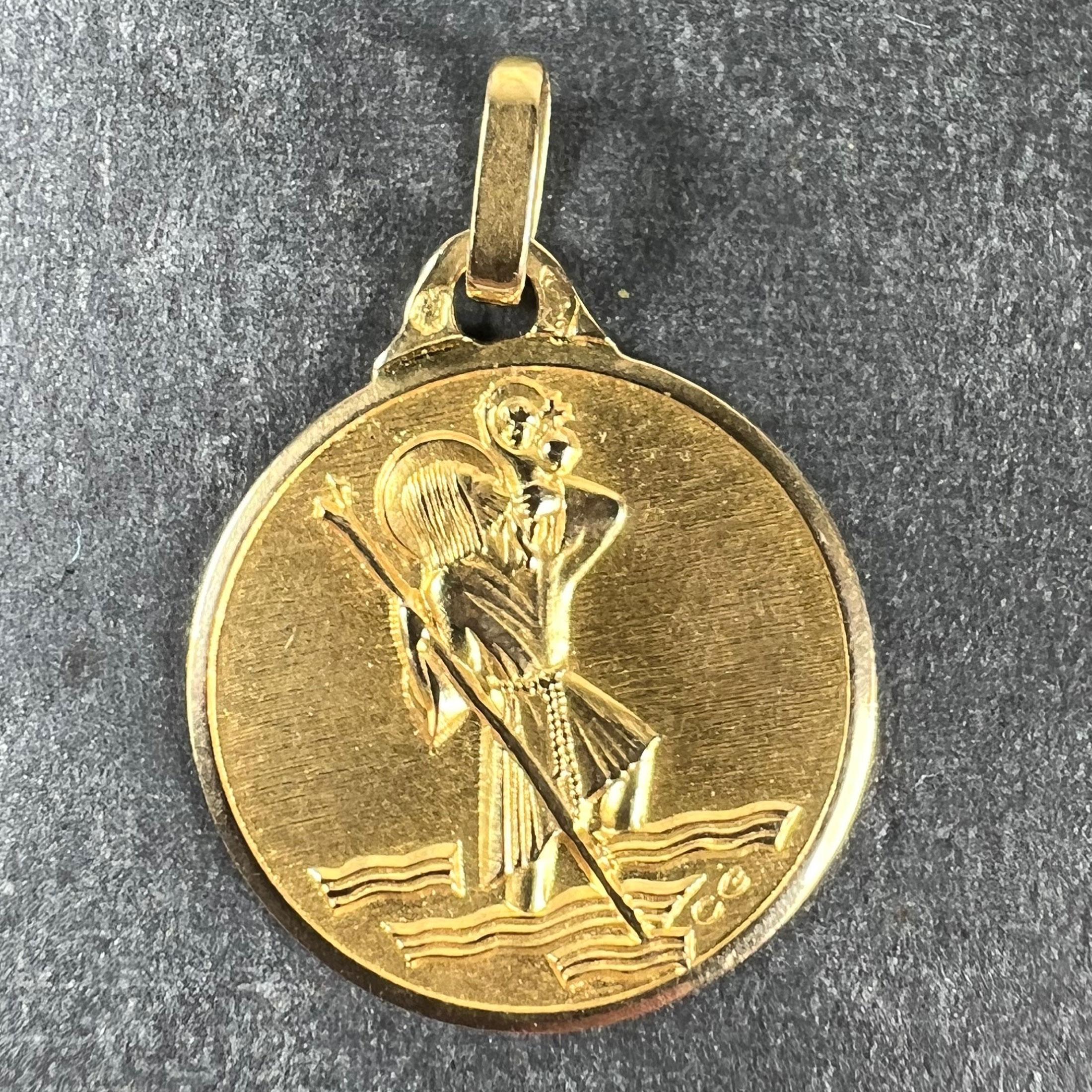 A French 18 karat (18K) yellow gold charm pendant or medal depicting St Christopher carrying the infant Christ across the river. Signed CG. Stamped with the eagle's head for 18 karat gold and French manufacture, along with an unknown maker's