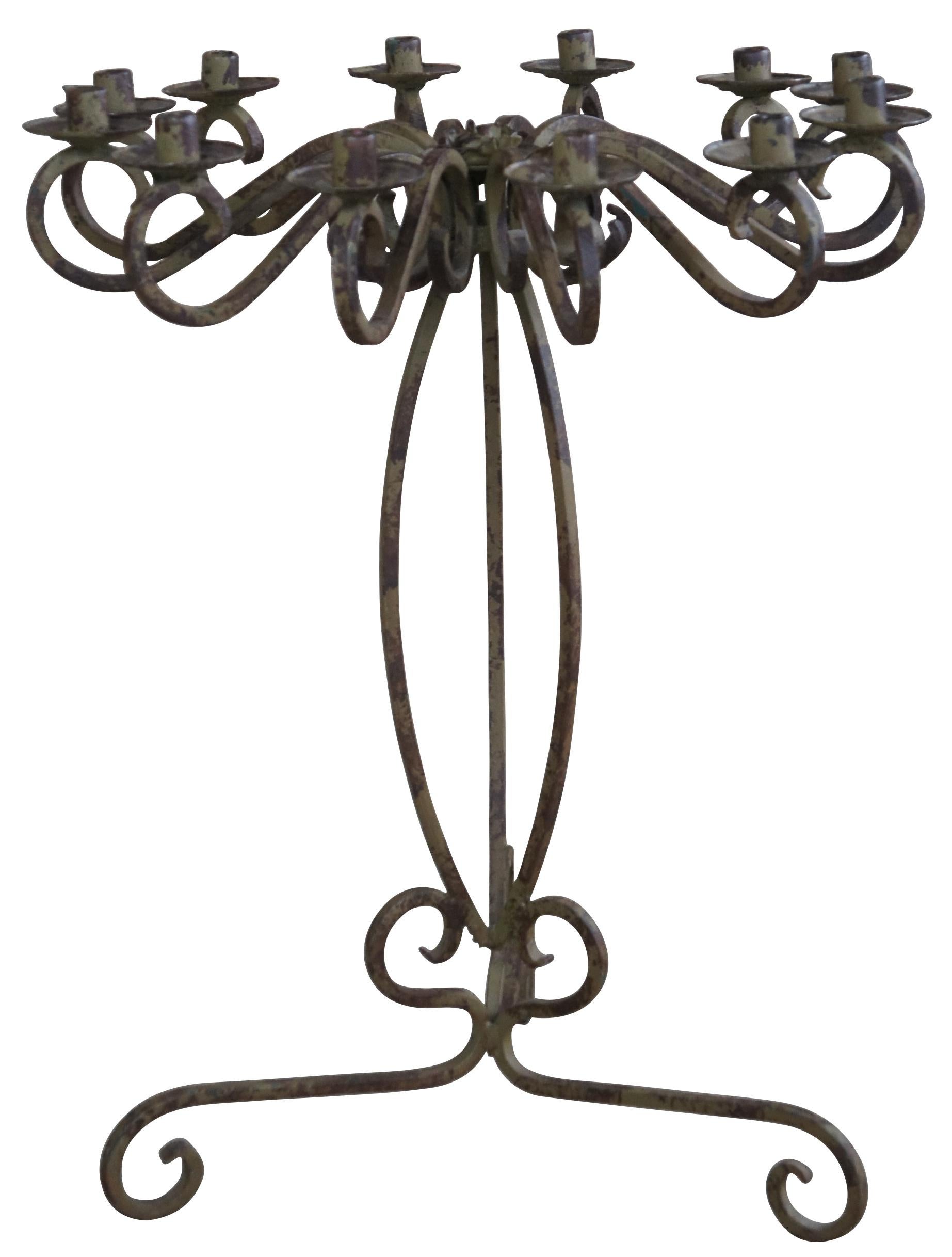 20th Century French or Gothic inspired 12 light candelabra. Features a scrolled design with pedestal and molded flower at the center. Each candle holder features a drip pan. The candelabra is finished in a rustic green patina and painted in a