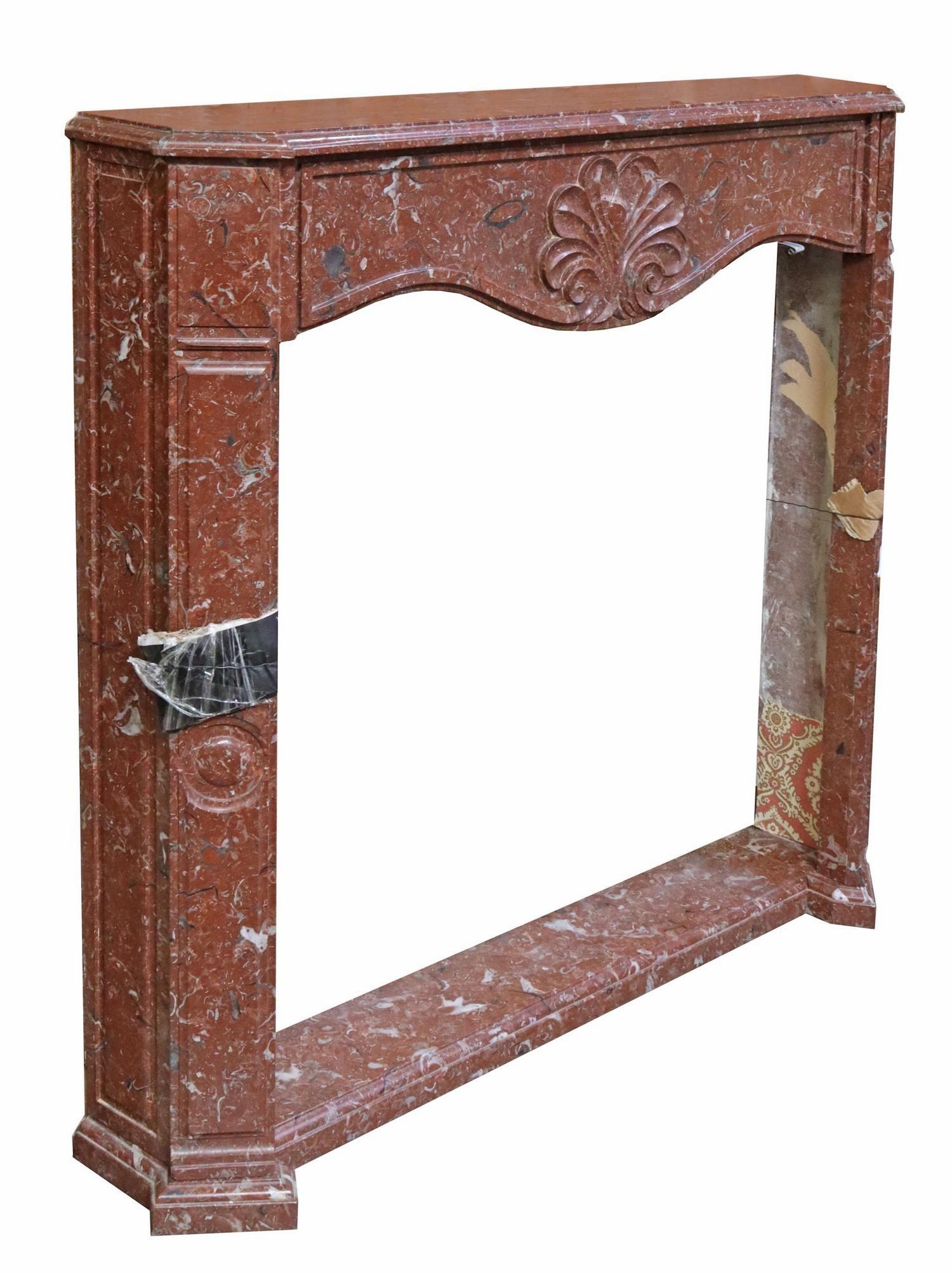 Continental red marble fireplace surround, early 20th c., having molded mantel shelf, over shell carved apron, pilaster corner supports, rising on plinth base.

Dimensions
 approx 51.5