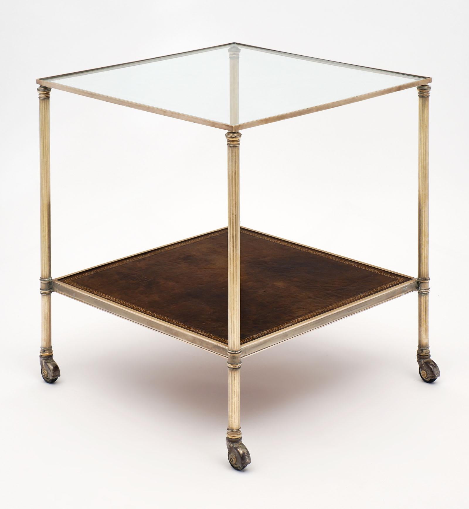 Fine French vintage side table with leather shelf and gilt polished brass structure. This piece is supported by original casters and boasts a clear glass top. The bottom shelf is covered with embossed leather for a handsome touch!