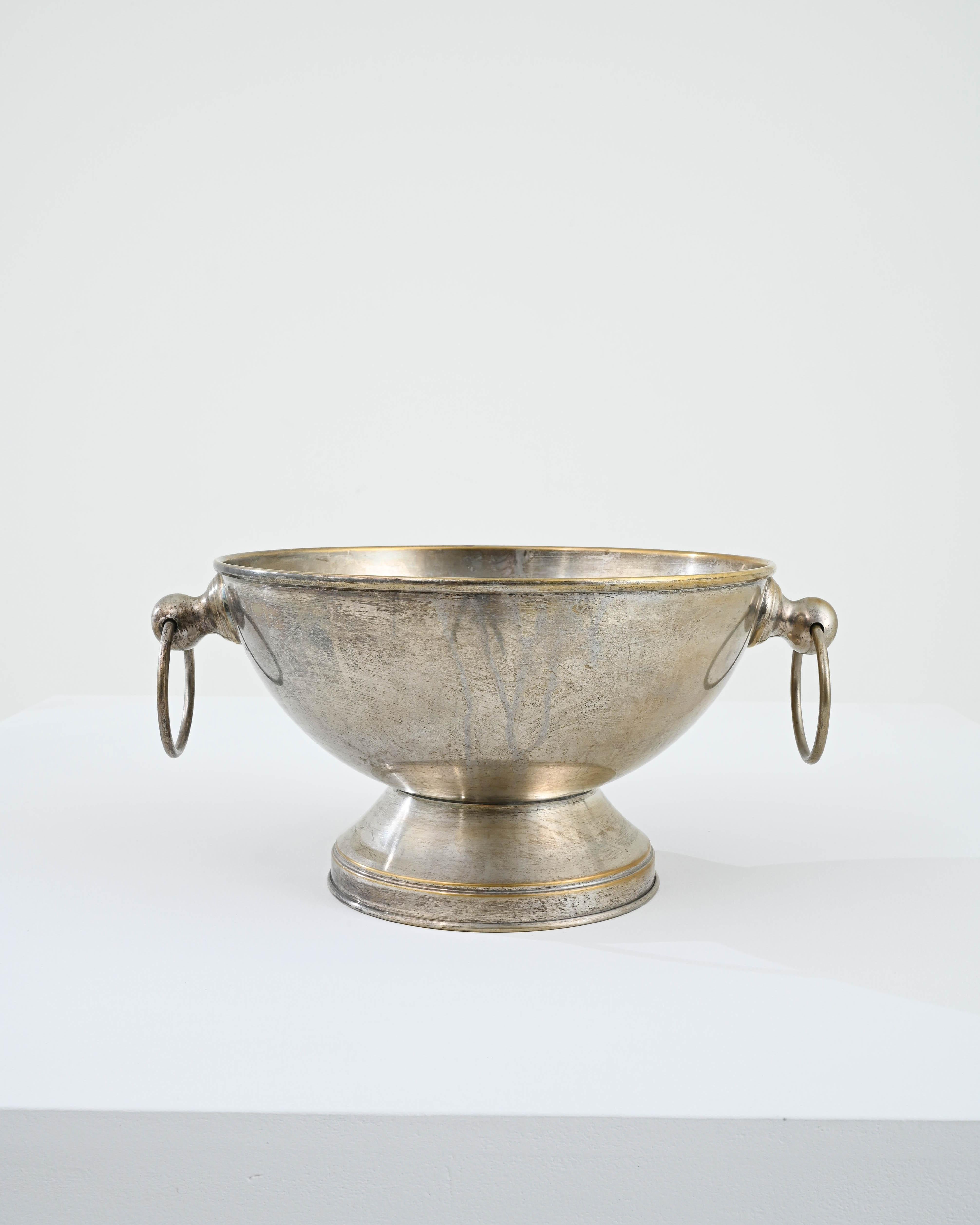 A brass bowl from early 20th Century France. A broad cup shape elevated on a low pedestal, the exterior surface has developed a captivating patina, muted golden brass melding with silver shine. The patinated finish, smoothed and tarnished, adds to