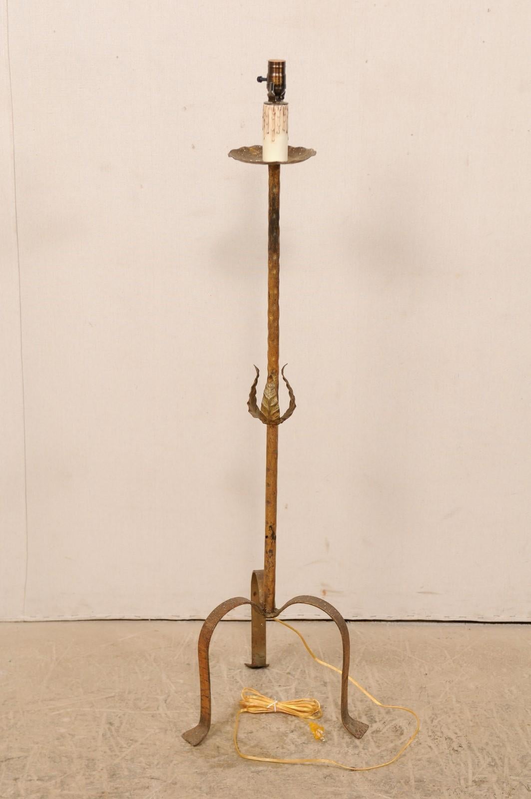 A French gold toned iron floor lamp from the mid-20th century. This vintage single-light floor lamp from France features it's original gold color over iron body, having a slender central post minimally adorn with three metal leaves wrapped loosely