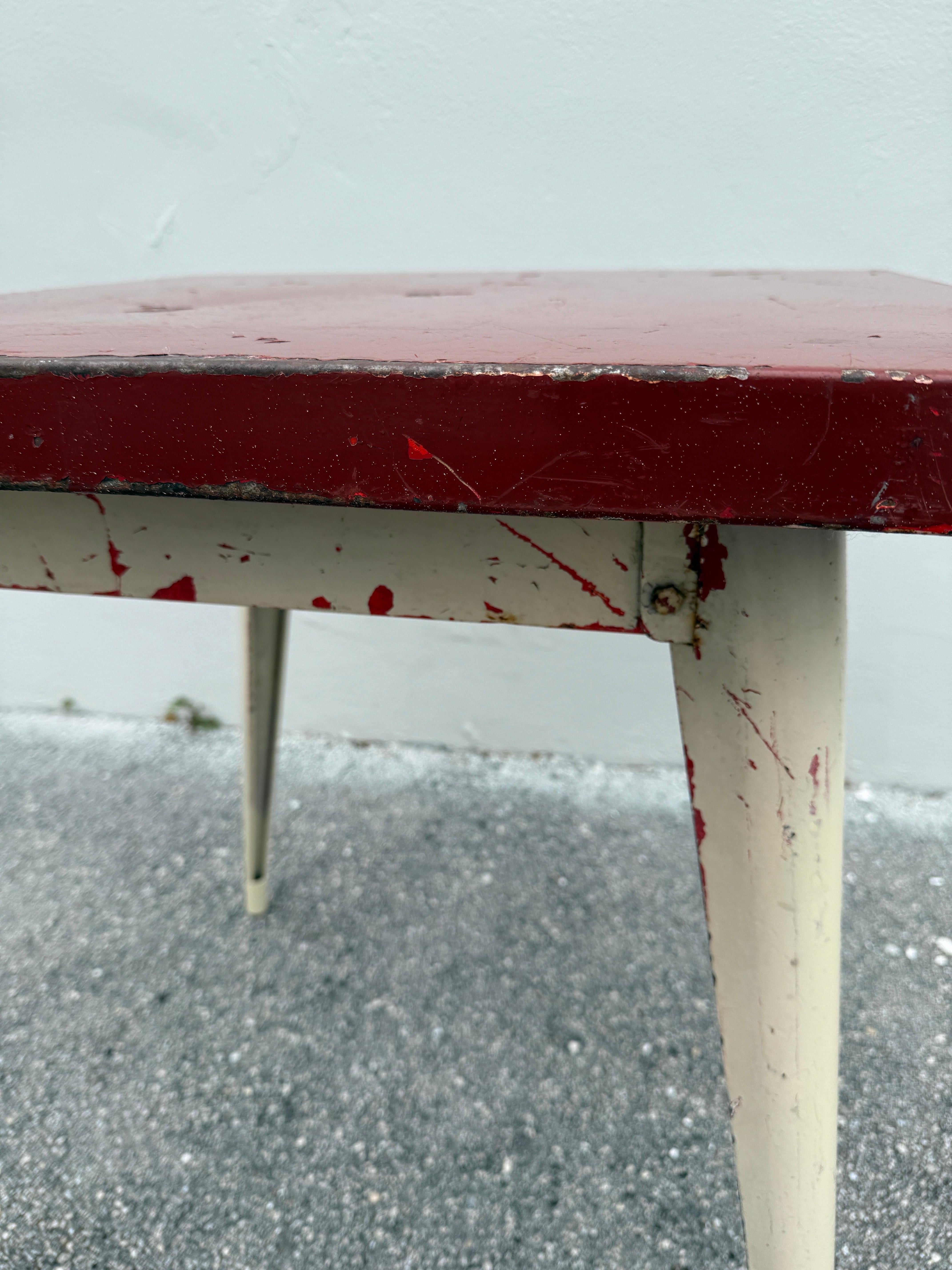 Il s'agit d'une table de bistrot française vintage de forme carrée conçue par Xavier Pauchard, mais très proche du style de Jean Prouve, avec des pieds en épée effilés et TOUTES les couleurs d'origine.  Une fantastique capote rouge foncé avec toutes