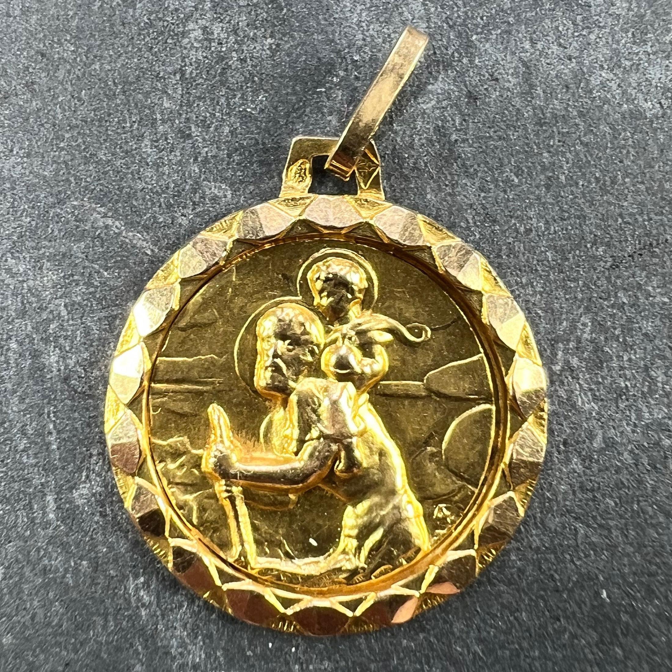 A French 18 karat (18K) yellow gold charm pendant depicting St Christopher as he carries the infant Christ across a river set in a faceted gold frame. Stamped with the eagle’s head for French manufacture and 18 carat gold, and an unknown maker’s