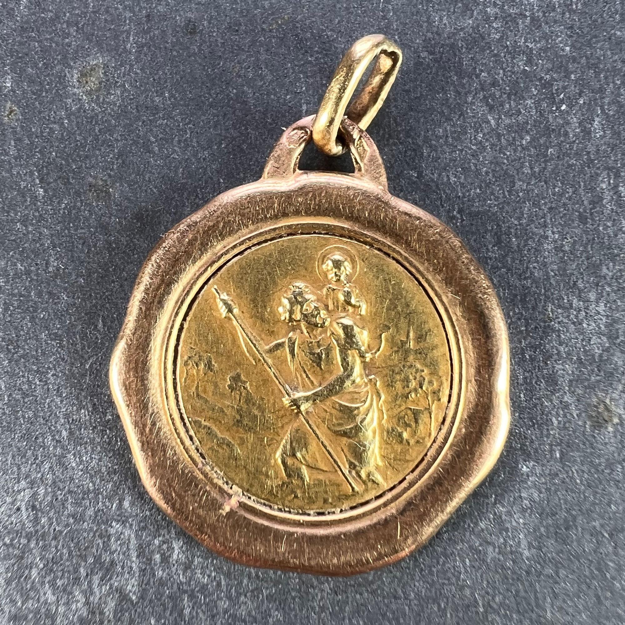 A French 18 karat (18K) yellow gold charm pendant depicting St Christopher as he carries the infant Christ across a river set in a wavy rose gold frame. Stamped with the eagle’s head for French manufacture and 18 carat gold, and an unknown maker’s