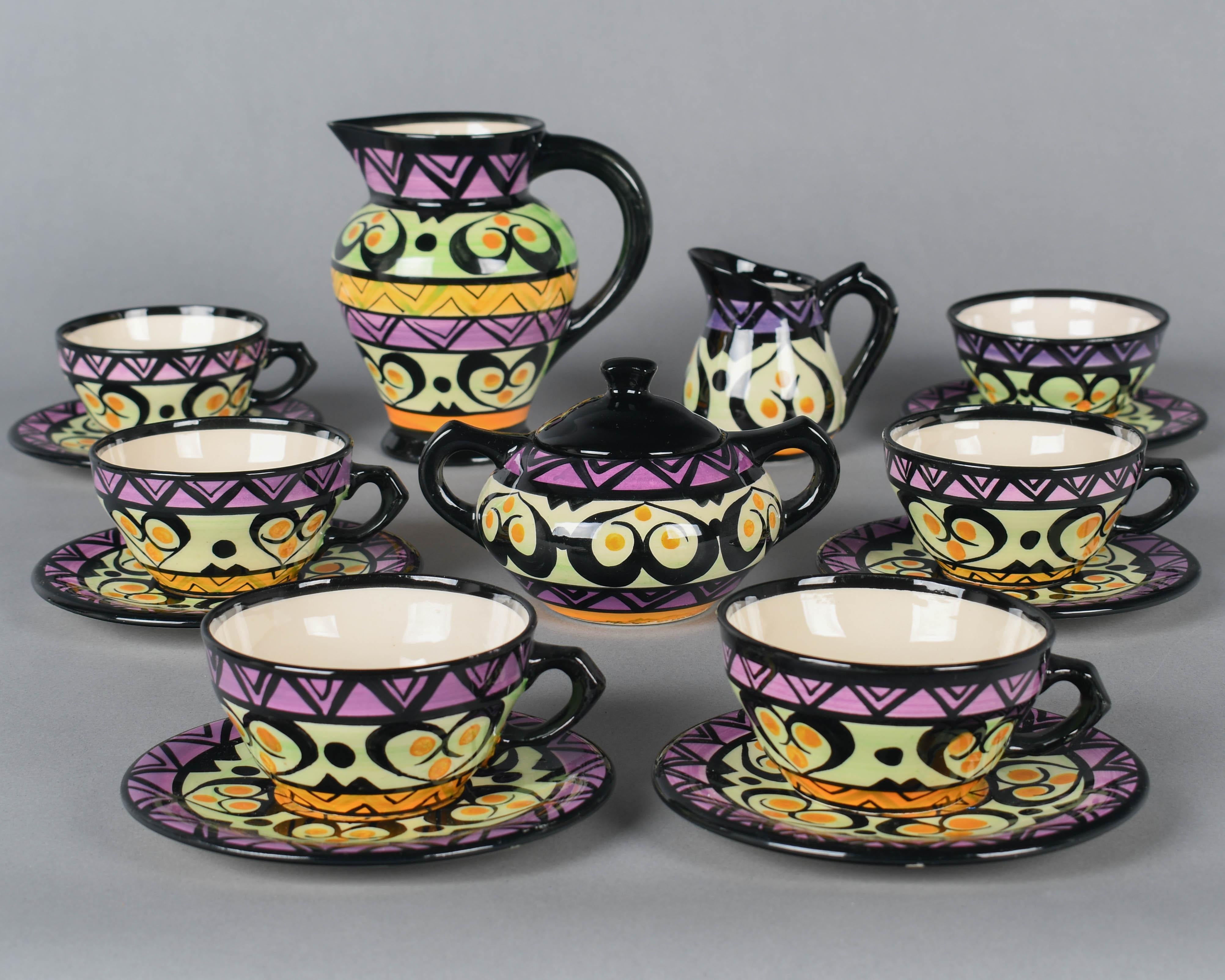 A Mid Century French ceramic tea set by St. Jean de Bretagne, hand-painted with a geometric design in bold colors of black, magenta, purple, orange and pale green. Set includes a milk pitcher, small creamer, sugar bowl and six cups and saucers.