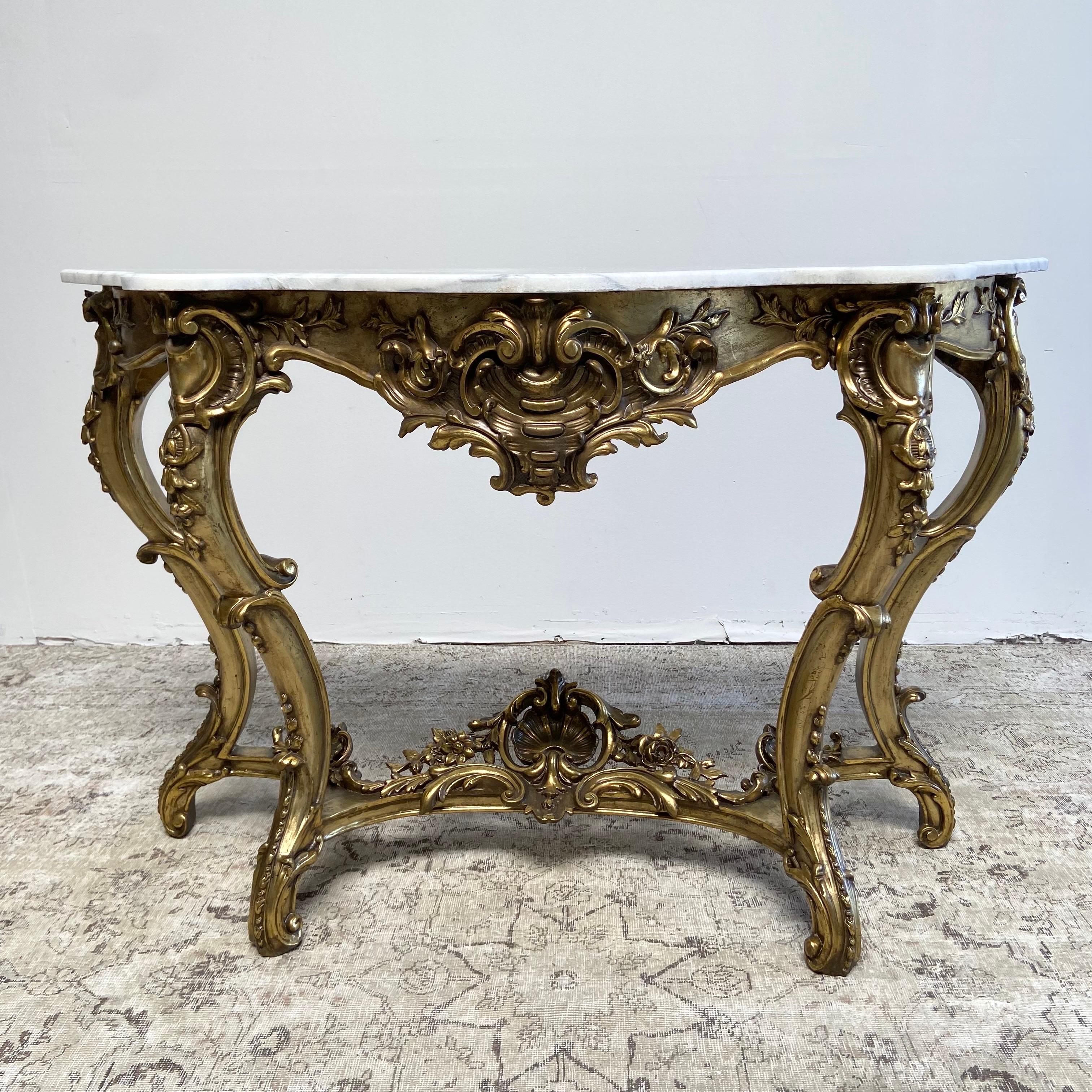 Free standing on 4 French Louis XV Style legs. A large cartouche with 3 large carved roses at the center of the stretchers, and highly carved florals on the front legs. Table has a dovetail construction. The marble top is a white color, with gray
