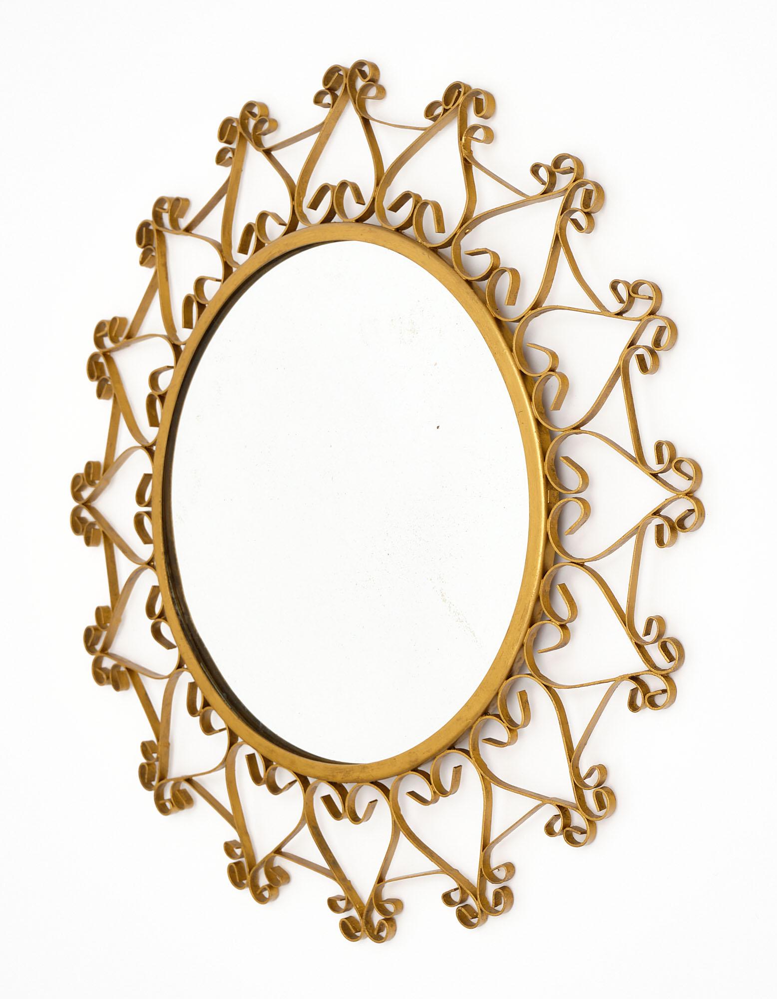 Mirror made of gilded forged iron that has been gold-leafed. This vintage piece has a circular center mirror surrounded by the intricate sunburst metal work.