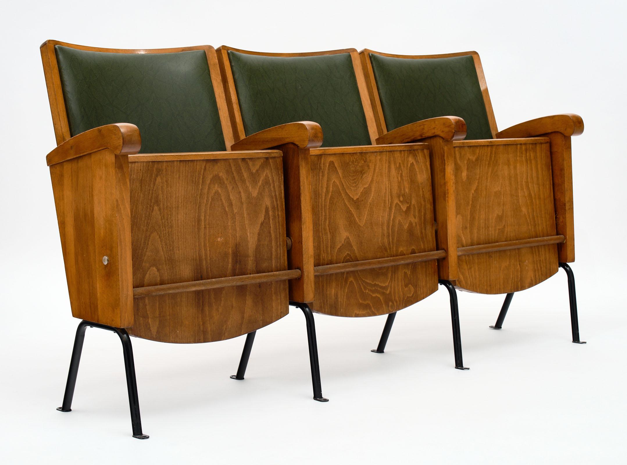 French vintage theater seats made of walnut and upholstered in the original green vinyl. The legs are metal. The row has three seats and the depth listed is when the seats are up. When down, the depth of the row is 24”. The height of the arms is