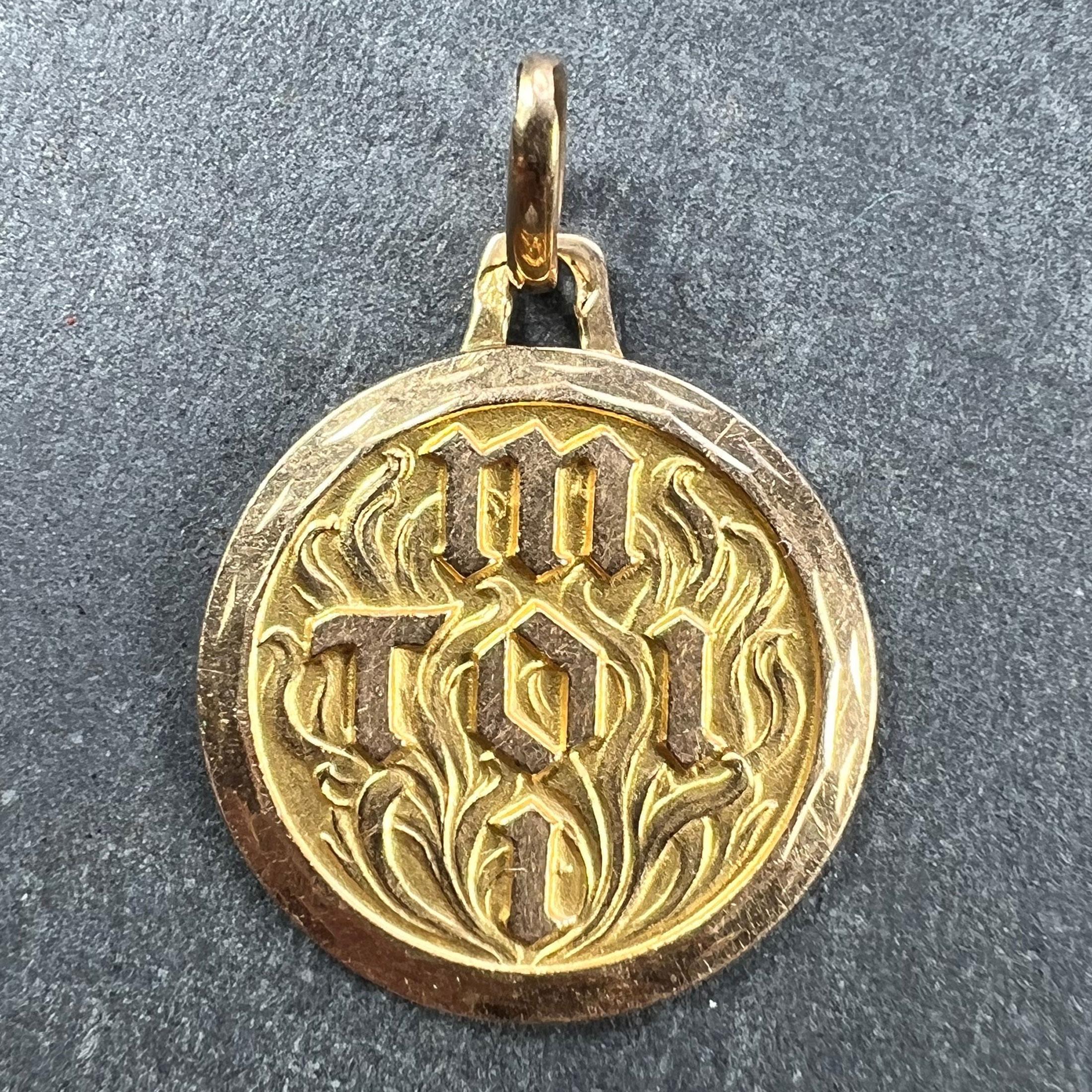 An 18 karat (18K) yellow gold Toi et Moi (You and Me) love charm pendant designed as a round disc with raised letters spelling Toi and Moi in a cross formation sharing the letter O. To the background a textured ground designed as the flames of love.