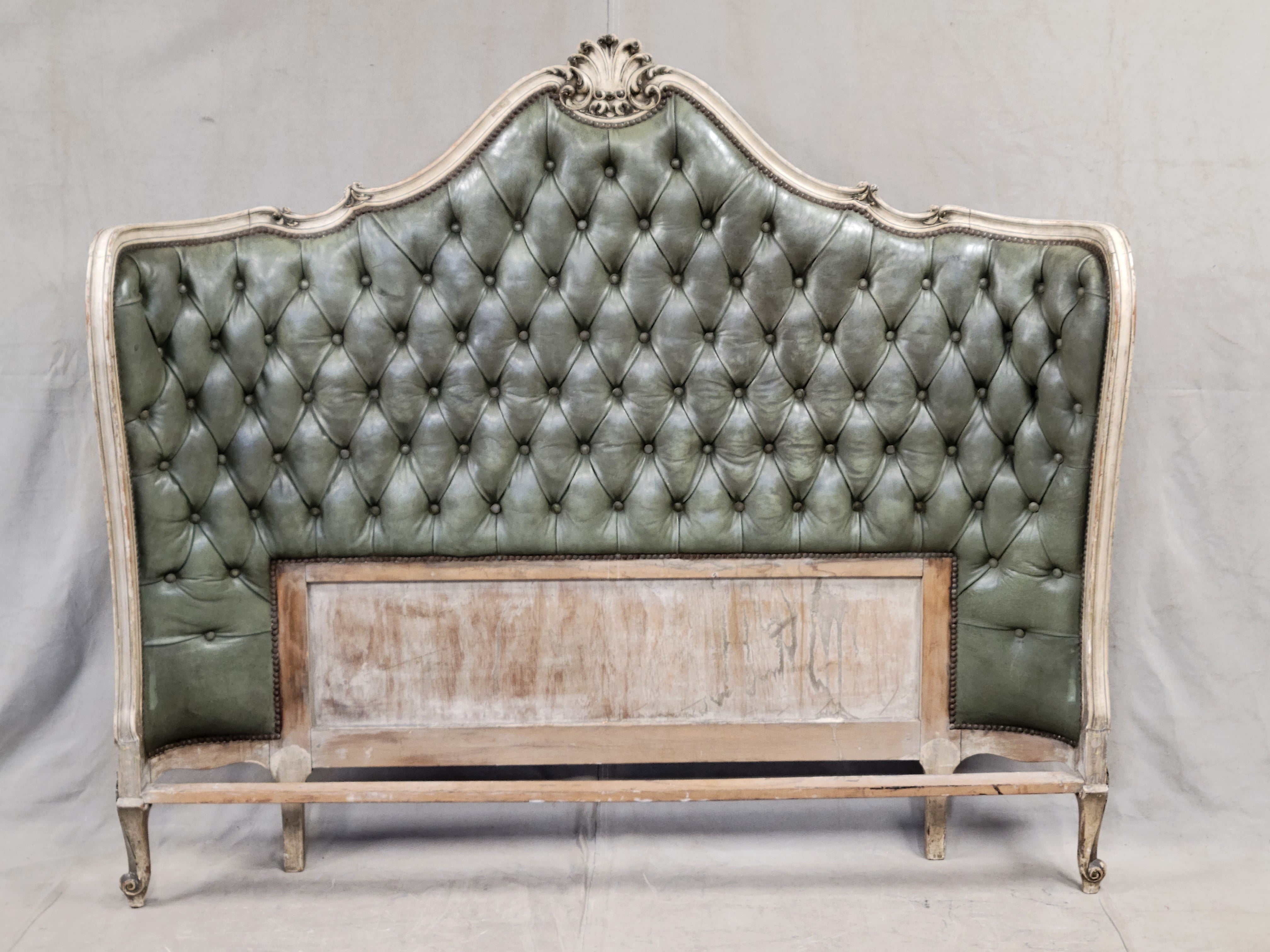 A gorgeous, vintage 1940s, or perhaps earlier, French tufted green gray leather headboard. The curve of the headboard envelopes the head of the mattress and gives this piece such character. Note the beautifully carved center fleur element and curved