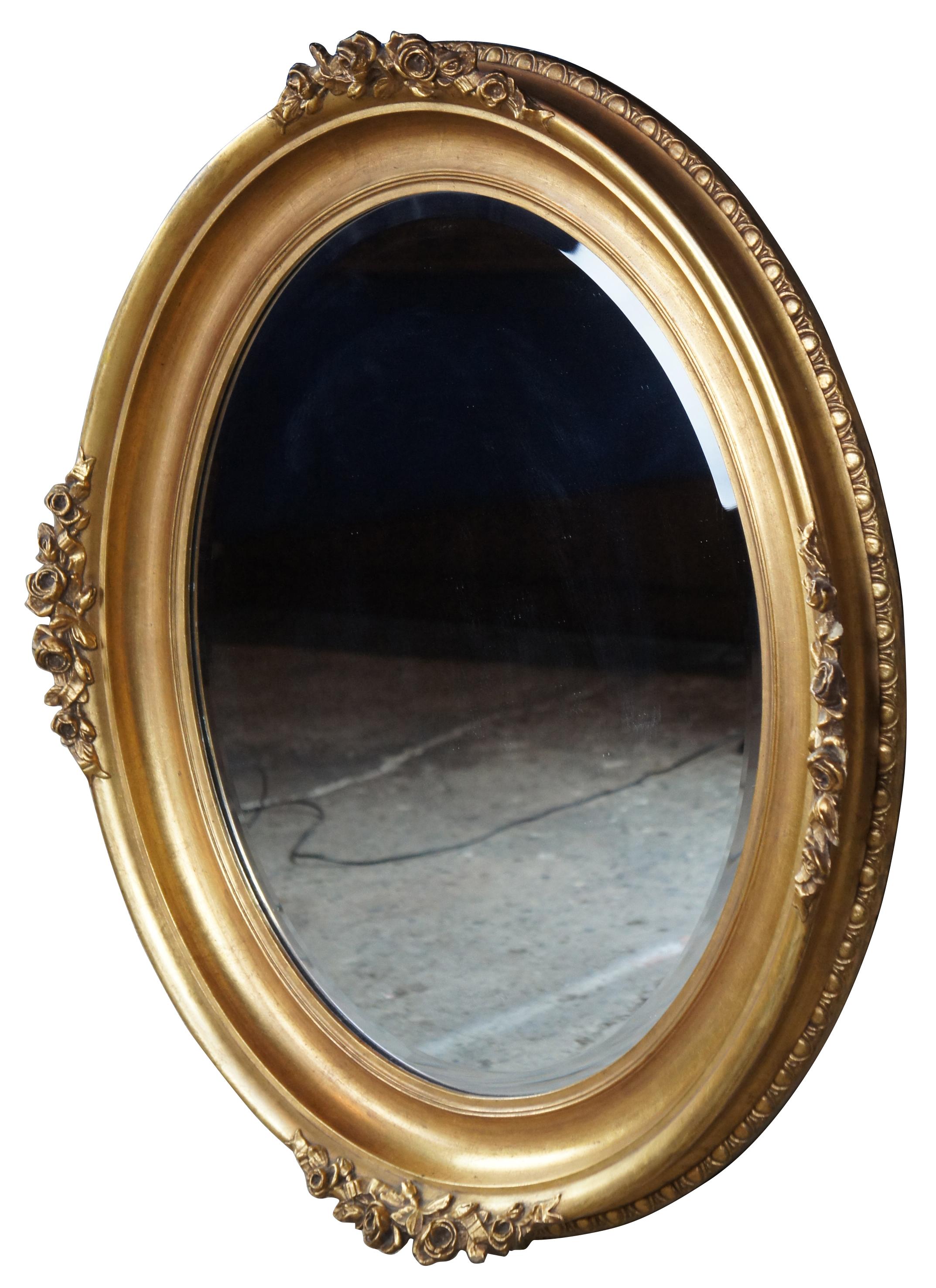 A mid-20th century Victorian inspired mirror. The oval frame features gadrooning trim along the back edge and floral roses and ribbons accents carved along the front edge in gesso. Measures: 35
