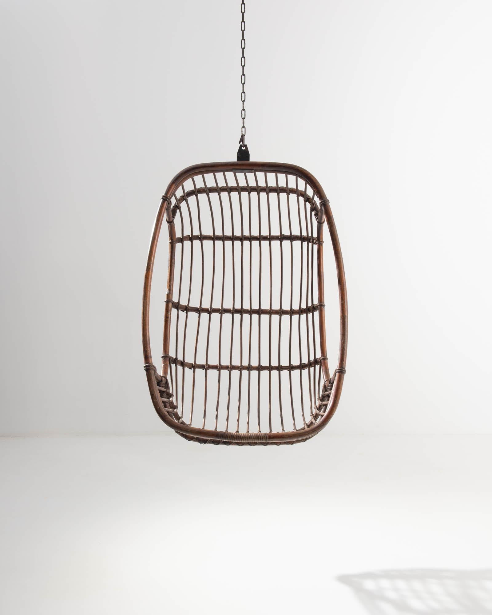 A rattan hanging chair made in 20th century, France. With a thick rattan frame, thin curved spindles, and neatly woven wicker lashings, this chair presents a sumptuously curved form that gently cradles the body in a way that only an artisanal,