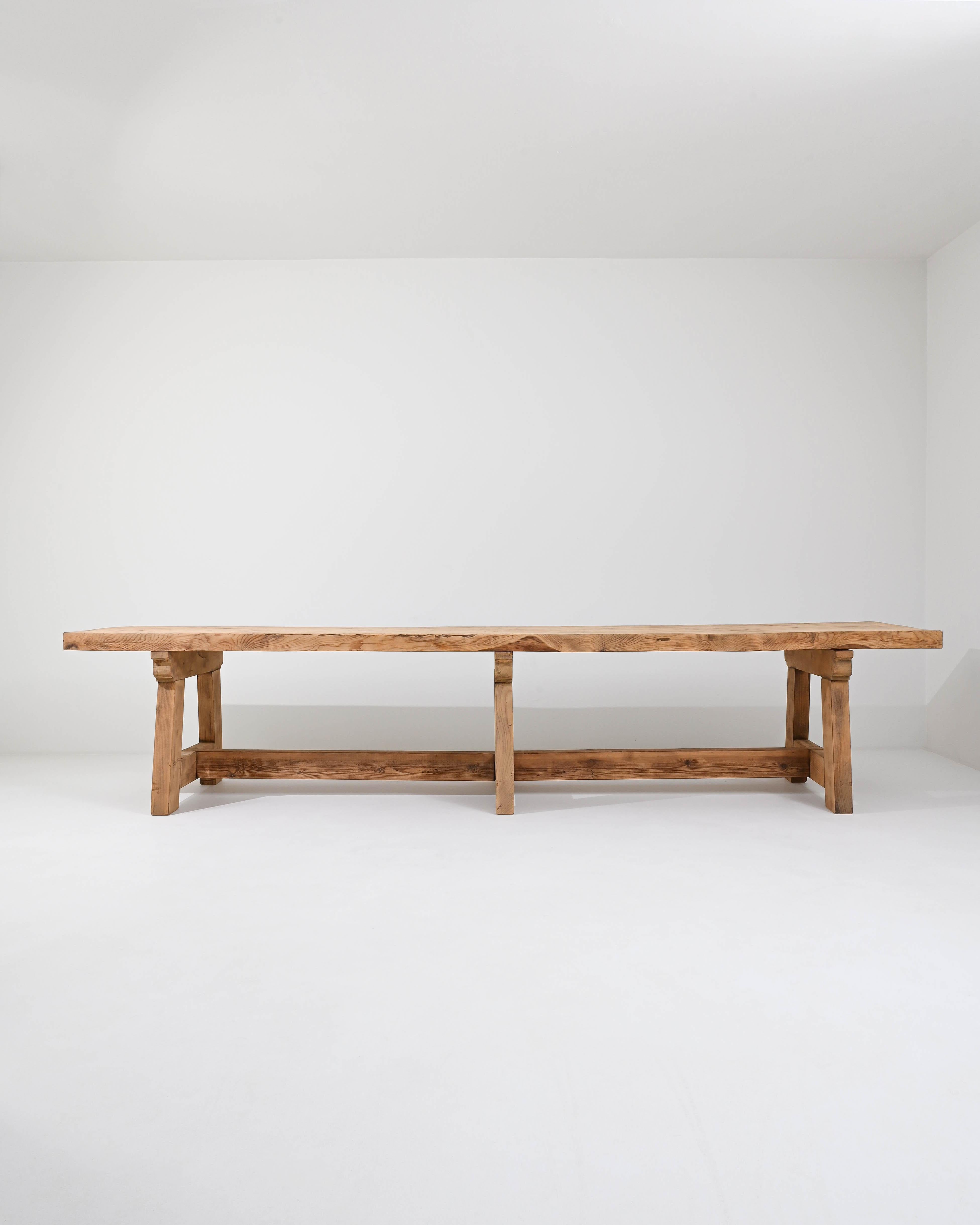 A wooden dining table made in France. Two staggering thick planks of wood combine to create a solid slab that composes the distressed top of this table. Weighty legs and stretcher bars form a geometrically pleasing latticework of joinery below,