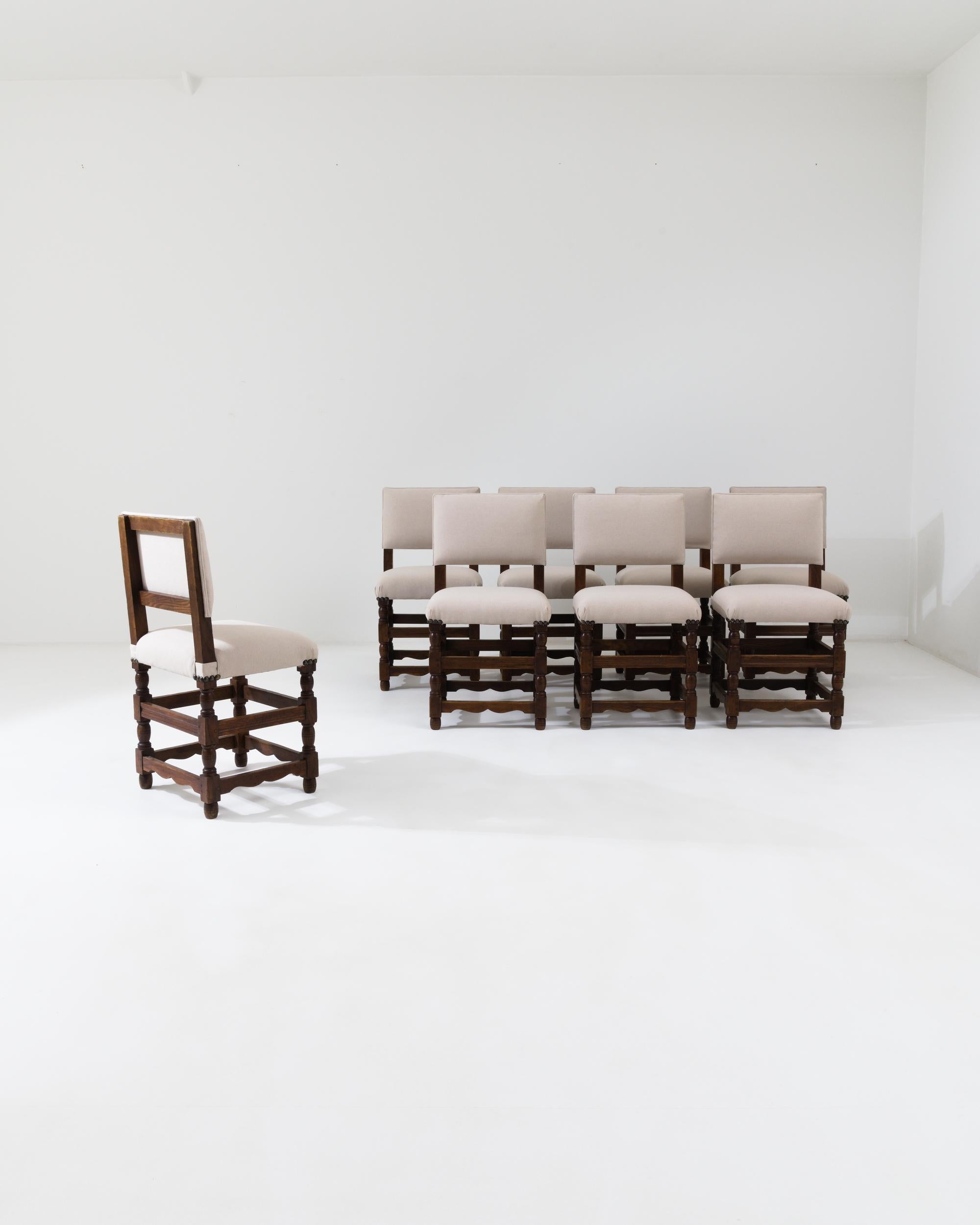A set of wooden upholstered dining chairs created in 20th century France. This congregation of eight dining chairs presents a picture of elegance and restrained beauty. Their clean, off-white upholstery allows their wood constructions, elaborately