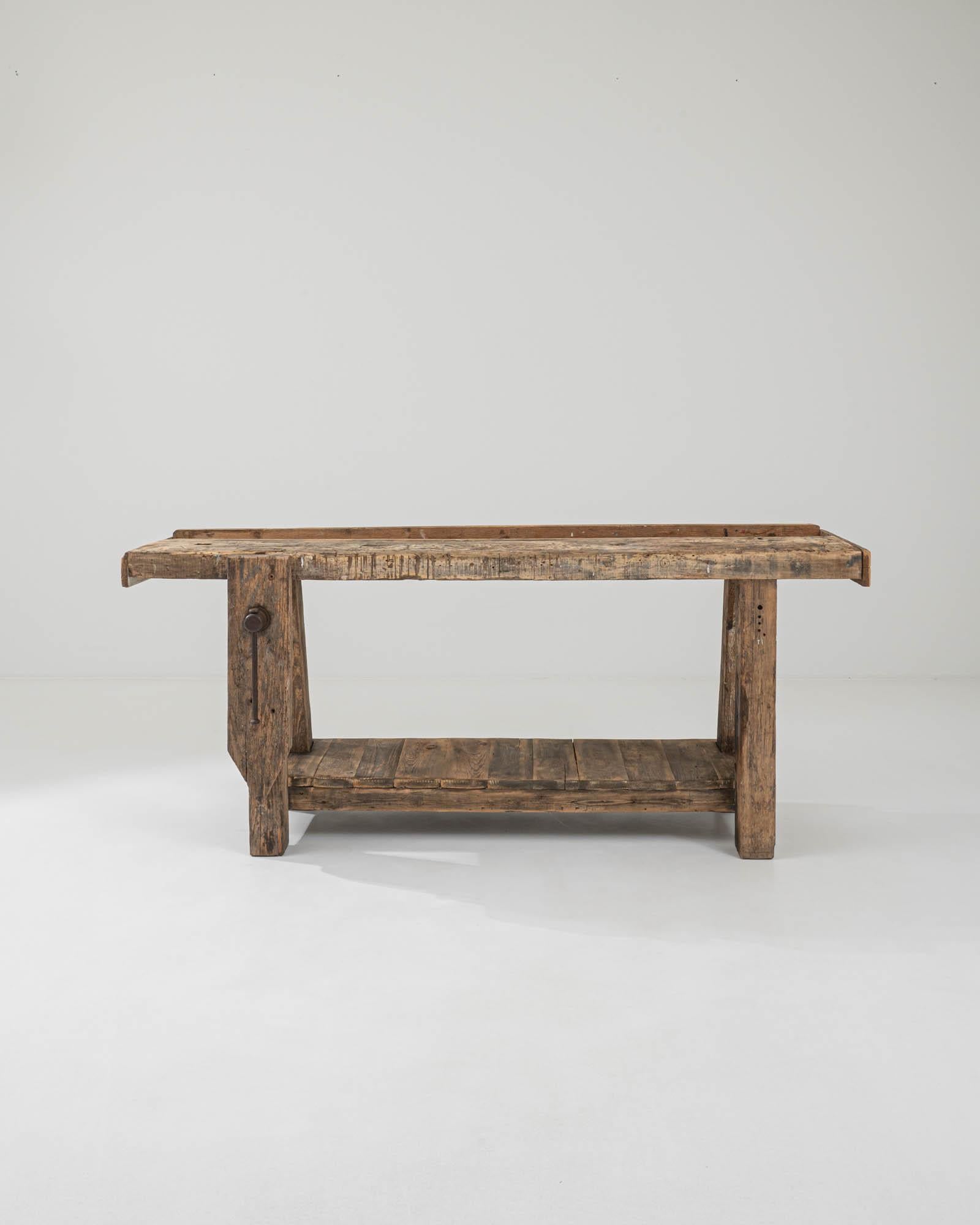 A wooden work table created in 20th century France. Weathered and time-touched, this distinguished workbench casts an aura of confidence and grand age. A simple and solid construction allows the compelling details upon it to shine. Dents, burns,