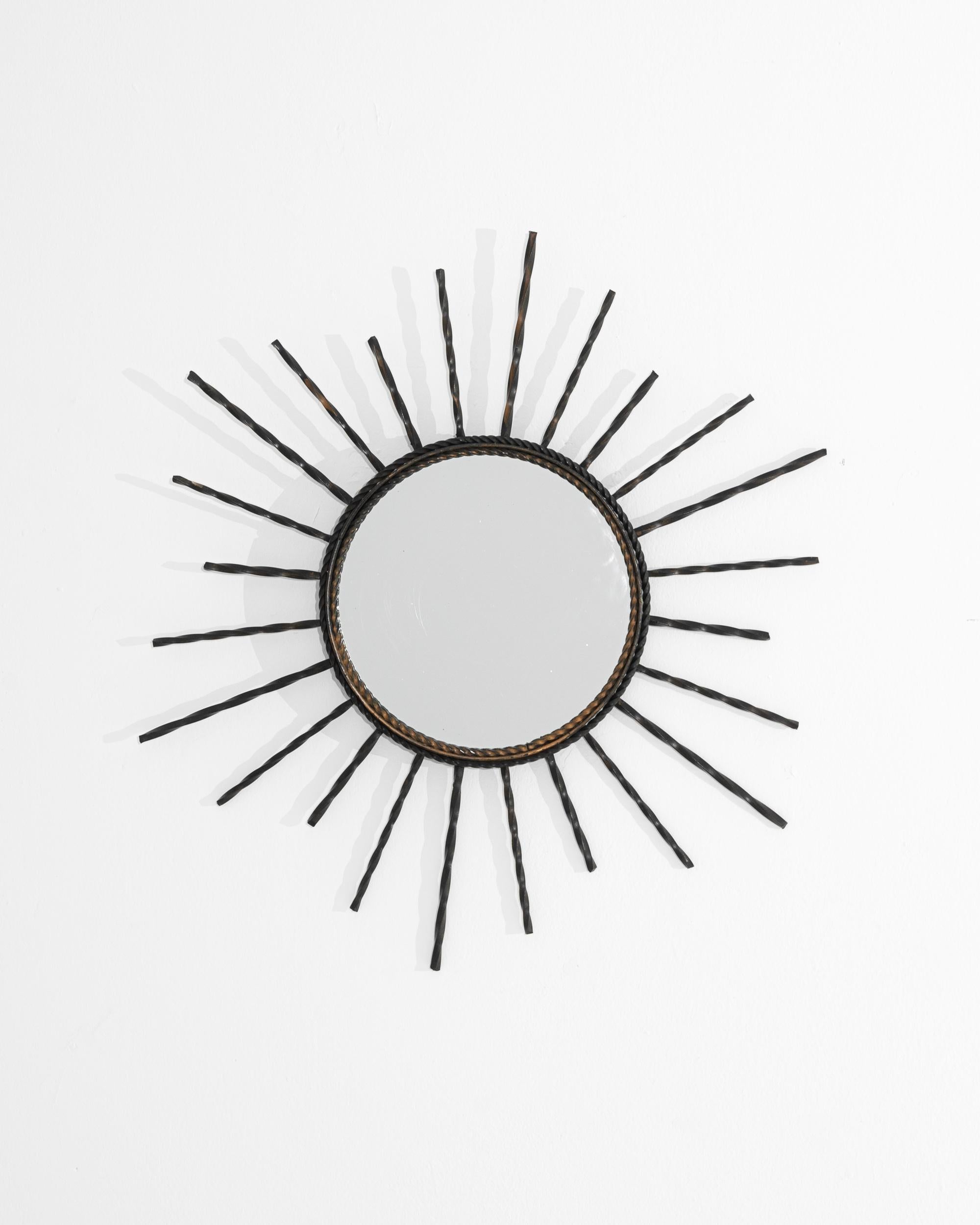 A vintage metal mirror from France. This small glass mirror is wreathed in an explosion of twisted metal lines. These energetic rays create a playful animation that plays around the mirror’s circumference. Promising to bring more grace and levity to