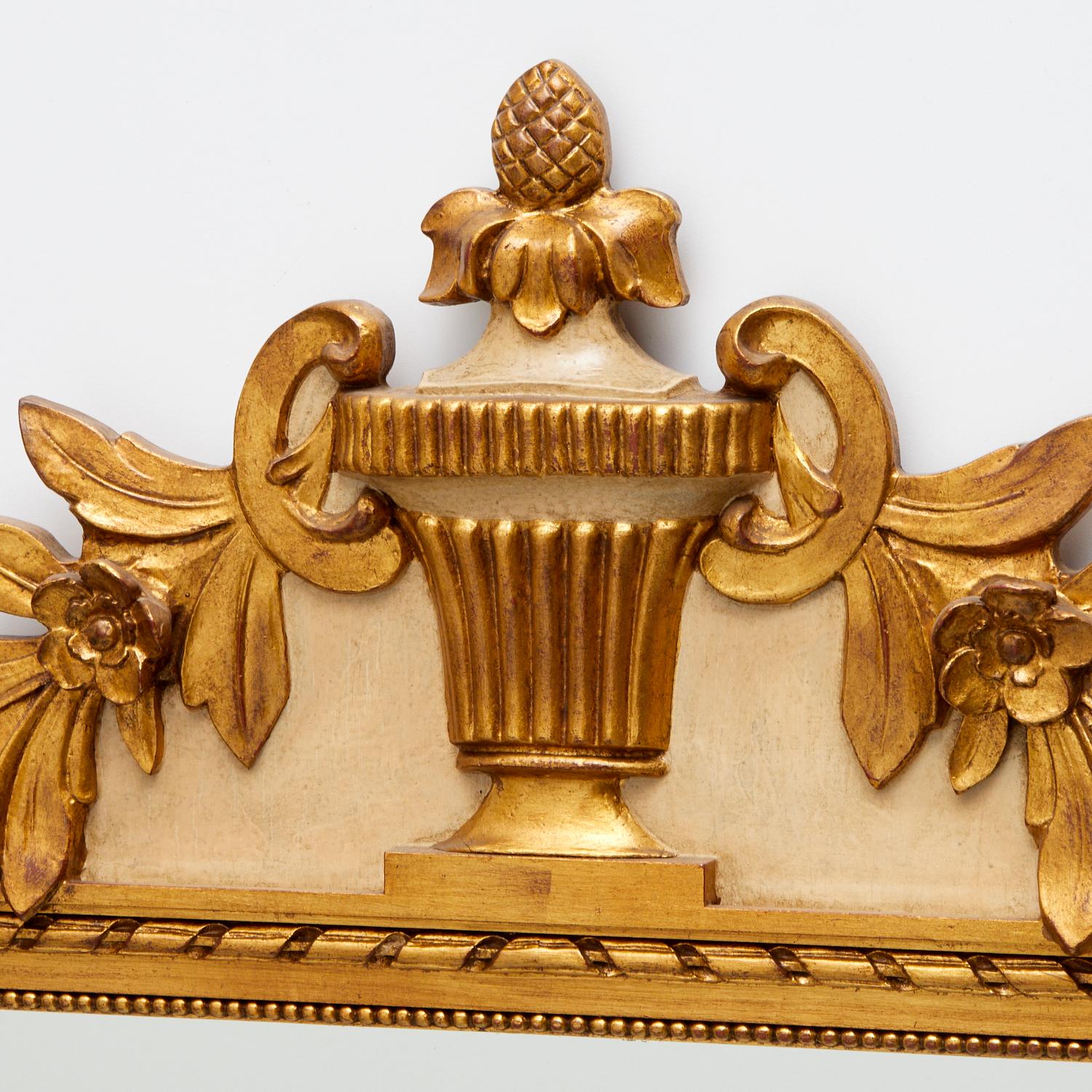 Vintage A.I.C. Friedman Bros. Miroir doré de style Louis XVI. Fond peint en crème sur la partie supérieure. Parcel doré avec un cimier sculpté en forme d'urne et des guirlandes florales, des torsades de corde et un décor de perles entourant le verre