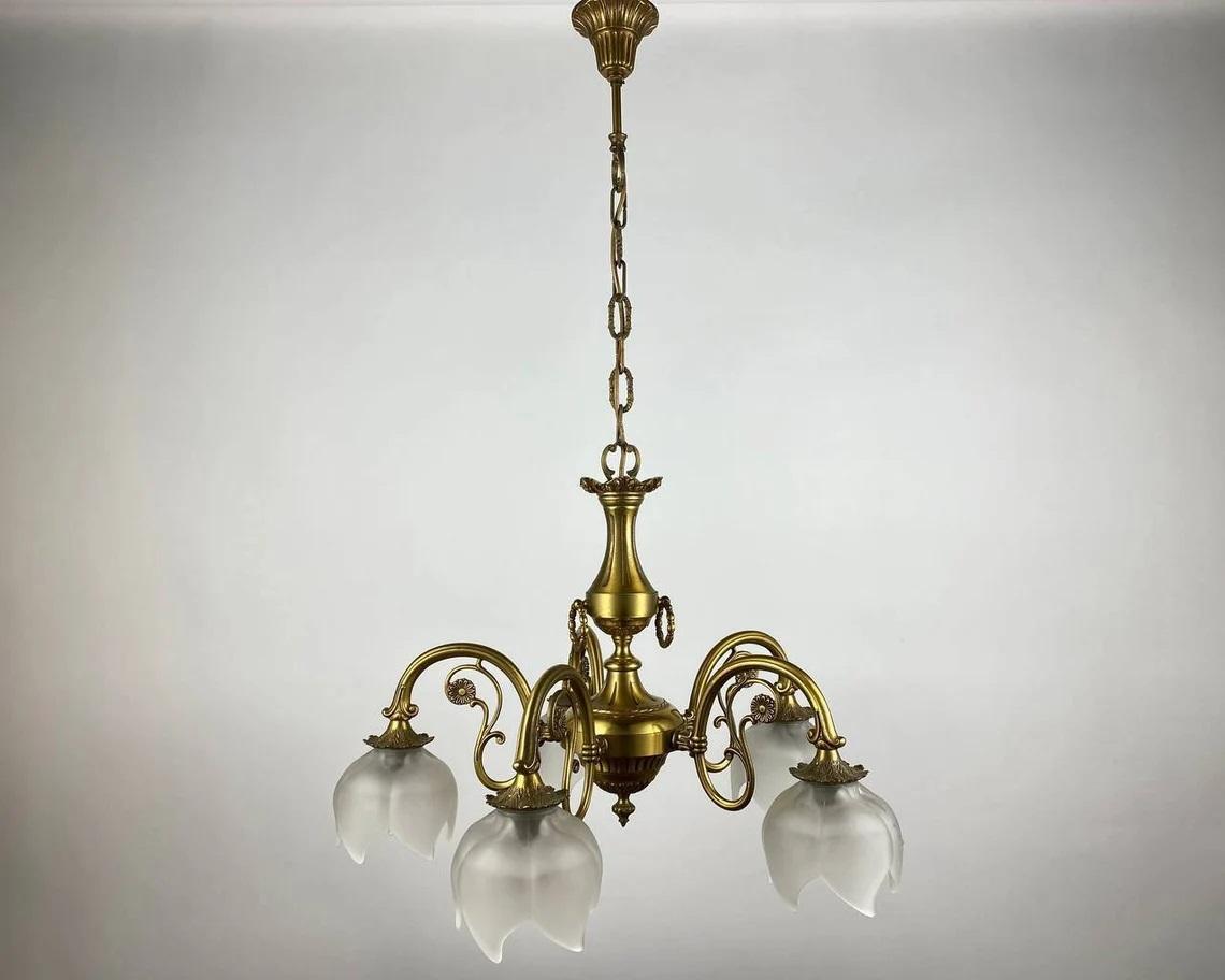 Vintage chandelier with 5 light points is the quality in every detail of the lighting fixture.

The cast brass frame of gold color looks solid, and frosted glass shades in the shape of a flower add lightness.

Matte shades pointing downwards