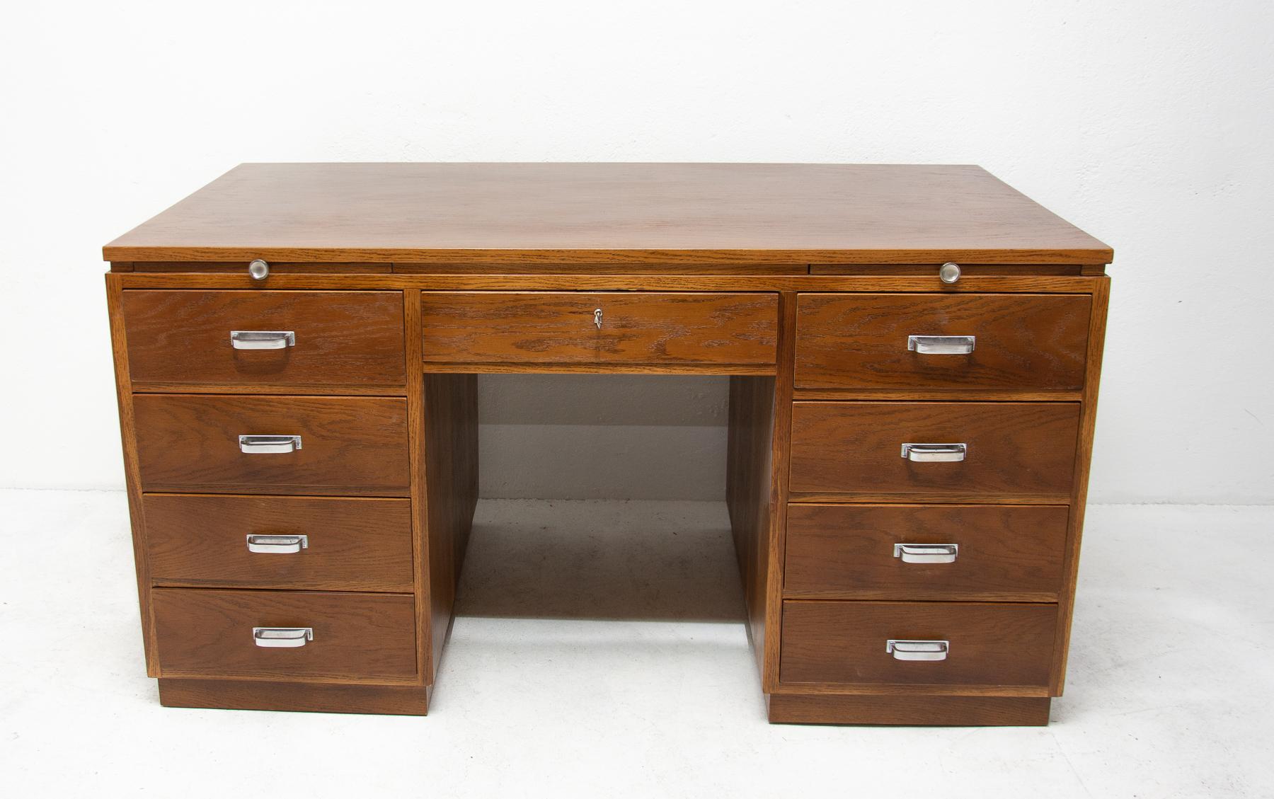 This massive functionalistic writing desk was made in the 1930s in Bohemia. It is veneered with oak, features four drawers with chromed handles on each side, and two pull-out plates. It is a very interesting design, typical for the functionalist