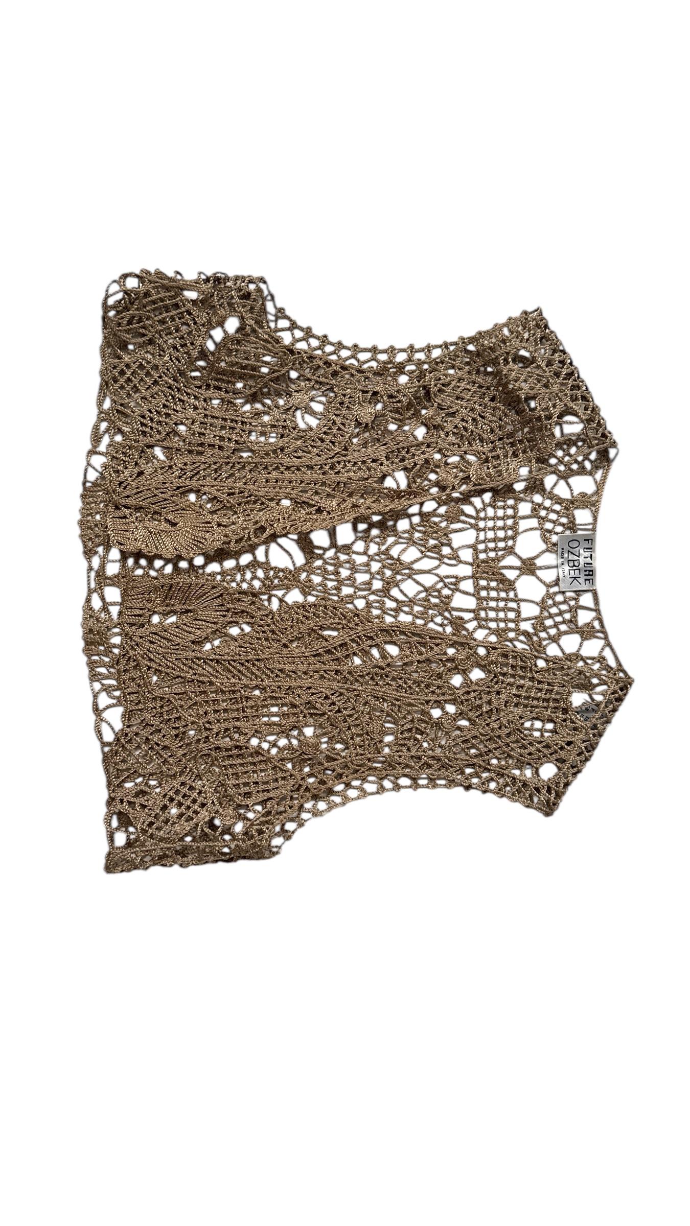 This exquisite gold-tone crochet vest by Future Ozbek embodies the eclectic glamour of Rifat Ozbek’s early 1990s vision. Featuring an intricate hand-crocheted design in metallic yarn, this sleeveless open-front vest showcases a sculptural, lace-like