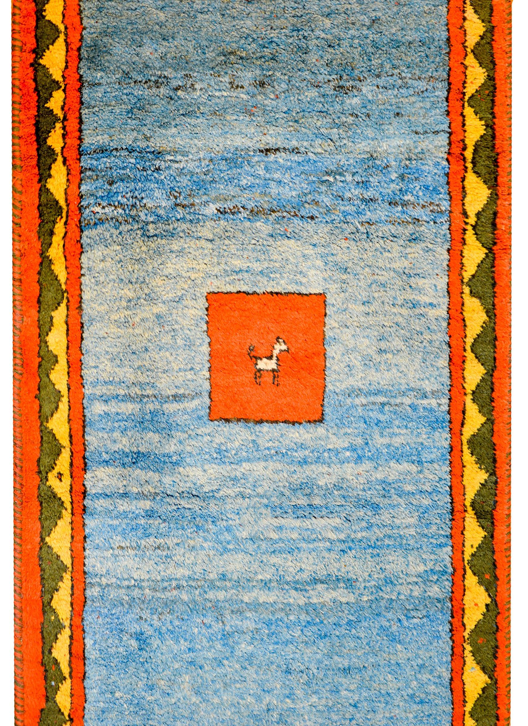 A wonderful and bold vintage Gabbeh rug with a variegated indigo field with an orange square in the center decorated with a goat, with additional goats in each corner. The border is complex with two matching red striped flanking a yellow and green