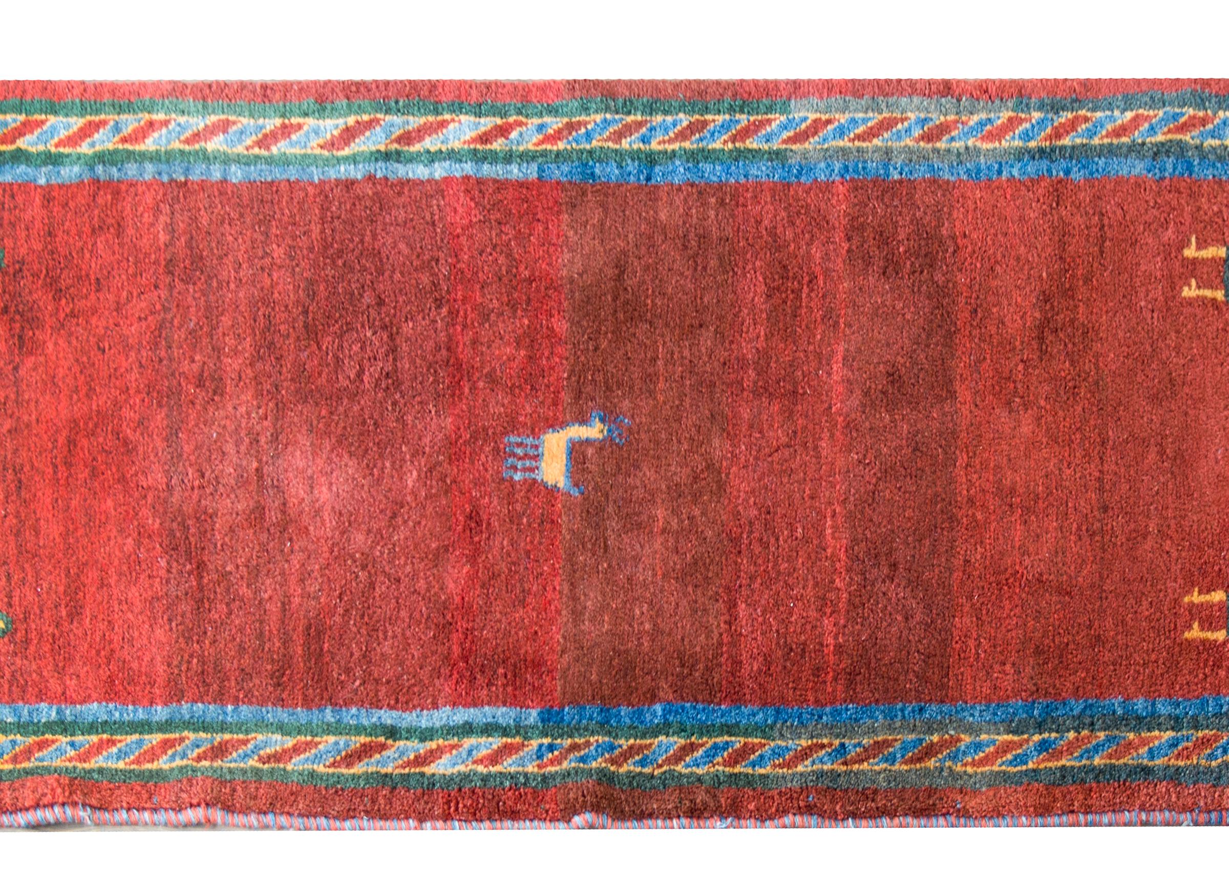 A remarkable late 20th century Persian Gabbeh rug with a wonderful abrash crimson field woven with a small goat in the center, and a small human figure in each corner, and surrounded by a geometric patterned border woven in crimson, green, gold, and