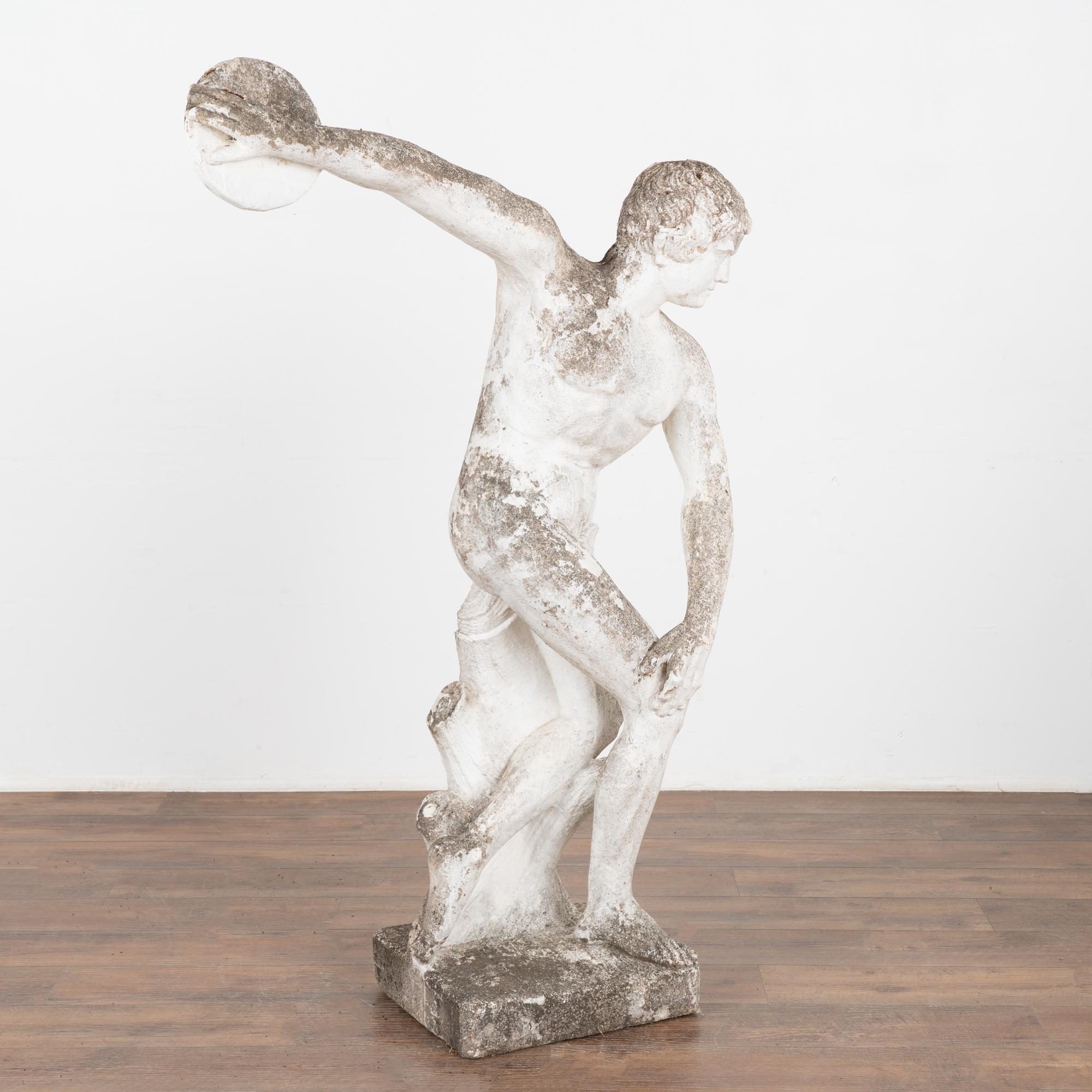 A garden sculpture of discus thrower made of limestone with paint remnants, reminiscent of an ancient Grecian sculpture.
The aged patina including distress to finish, wear, old lichen/stains, minor cracks, peeling paint all reflect generations of