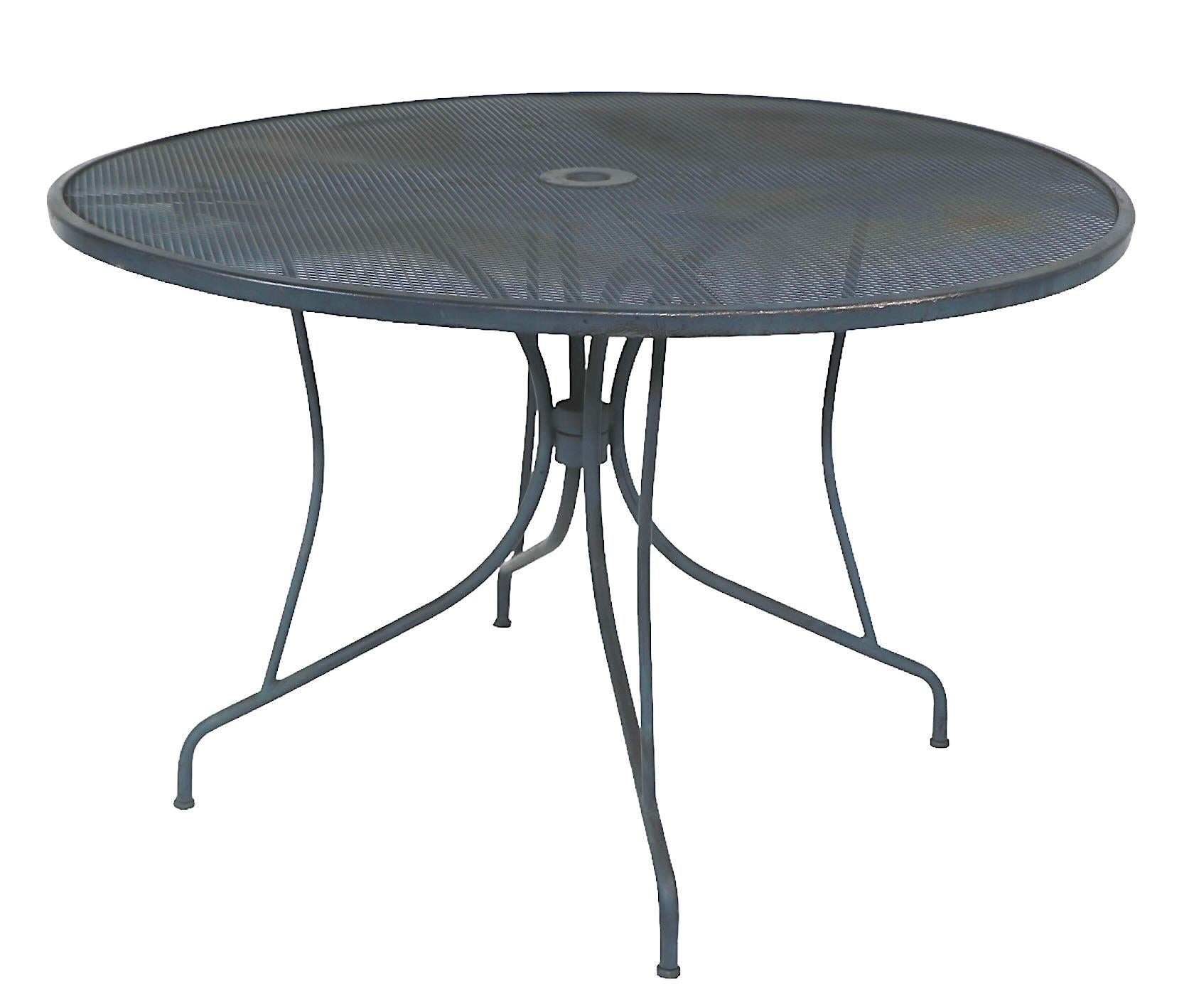 Vintage garden, patio, poolside cafe style dining table by Meadowcraft, in the style of Woodard, Homecrest etc. circa 1950/60's. Constructed of tubular metal, with a metal mesh top, features a center hole to accommodate an umbrella.  The table is in
