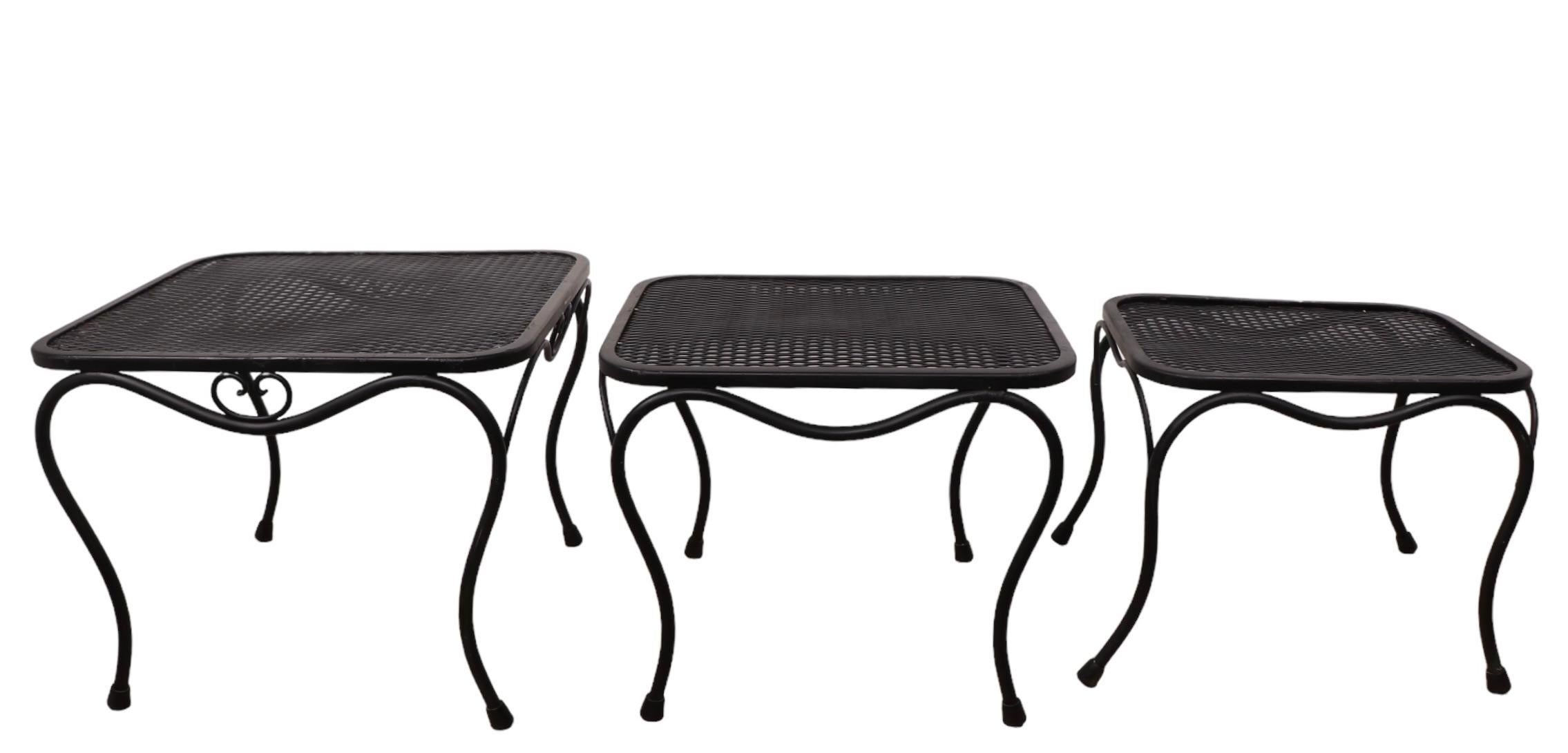 Set di tre tavoli da giardino, patio e piscina impilabili attribuiti a The Woodard Furniture Company, circa negli anni '70. I tavoli sono caratterizzati da  gambe curve stilizzate, con piani in rete metallica, sono di dimensioni graduali, il più