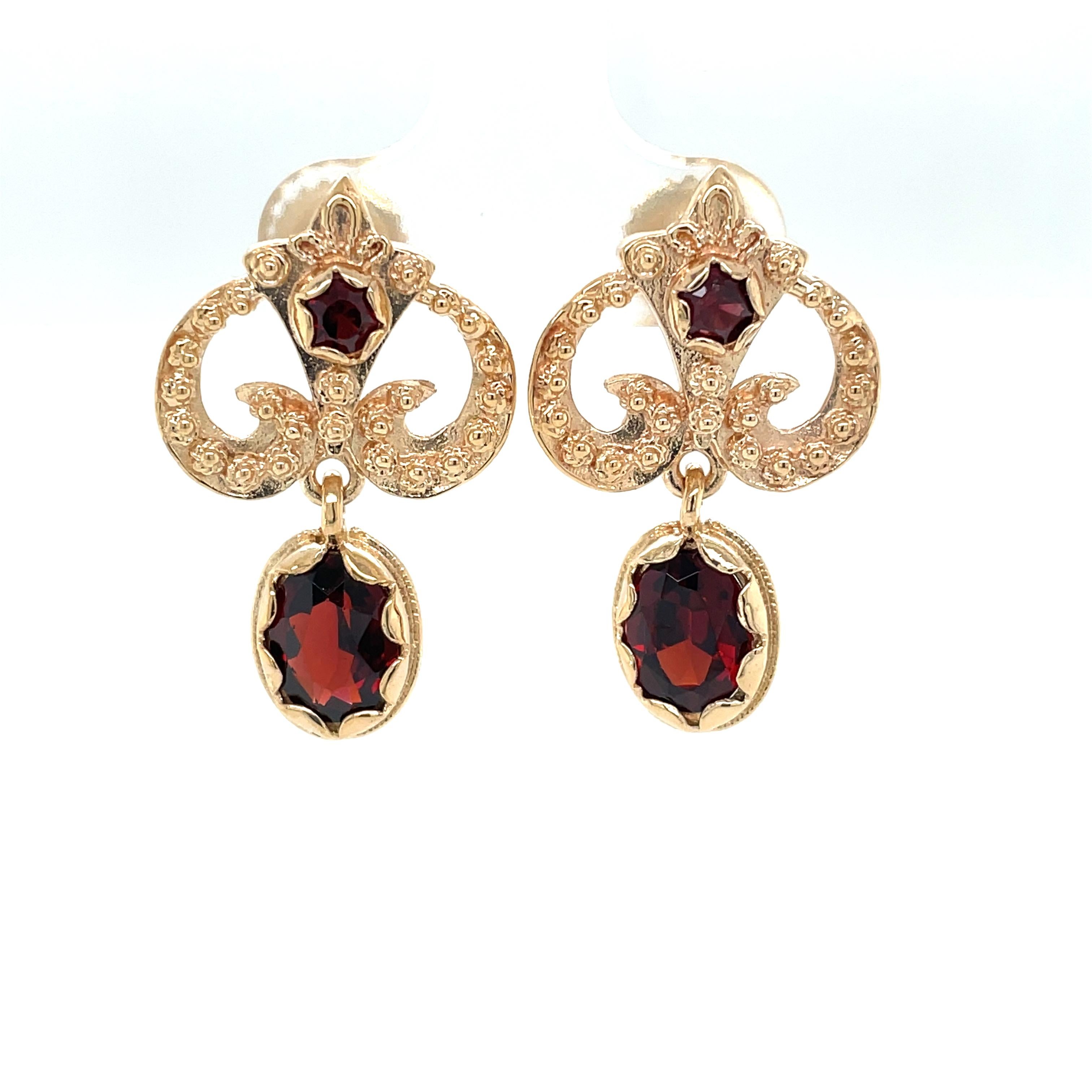 Rich red garnet is artfully bezel set in complementing 14 karat yellow gold which brings out the warmth of the 
gemstone. The Fleur delis upper dangle with its attractive open design is enhanced with textured gold and measures  approximately 5/8