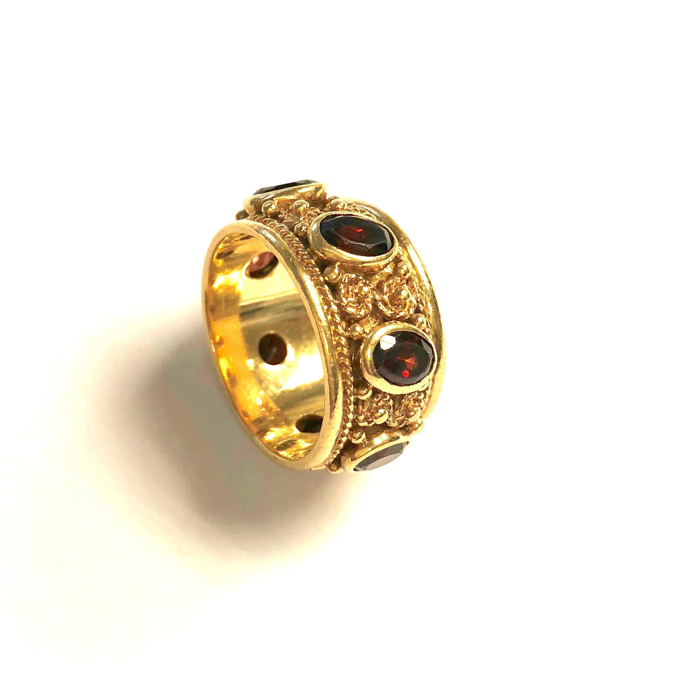 Unique 14K yellow gold band set with seven bezel set oval red garnets alternating with gold florets, accented by a rope style design. Approximate total garnet weight: 7.0ct. 
Size: 7
Width: 11 mm ( 7/16