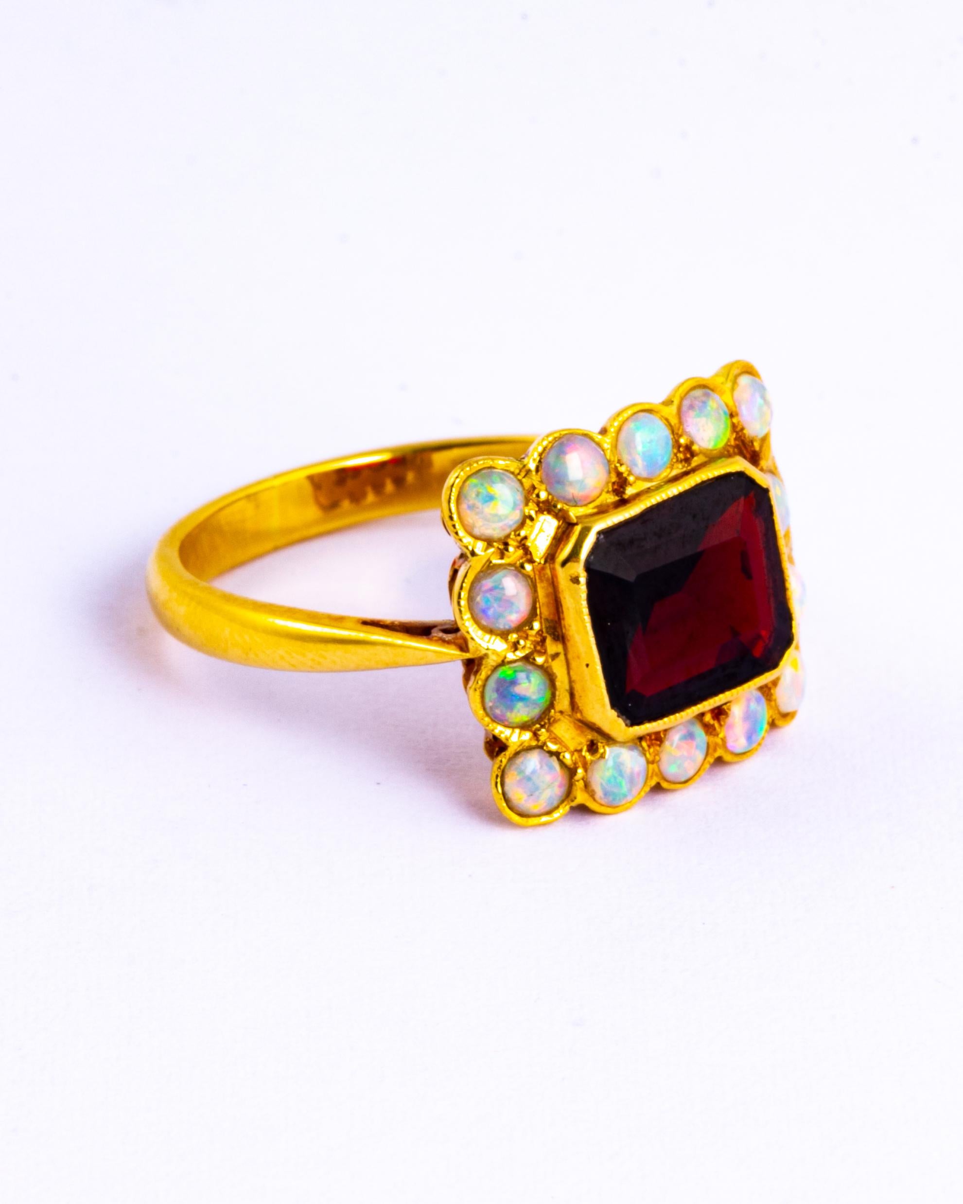 This striking ring holds an emerald cut garnet measuring approx 2carats and surrounding it are 14 shimmering opals. All the stones sit flush within the 18ct gold. Made in Chester, England. 

Ring Size: R 1/2 or 9
Panel Dimensions: 14x16mm

Weight: