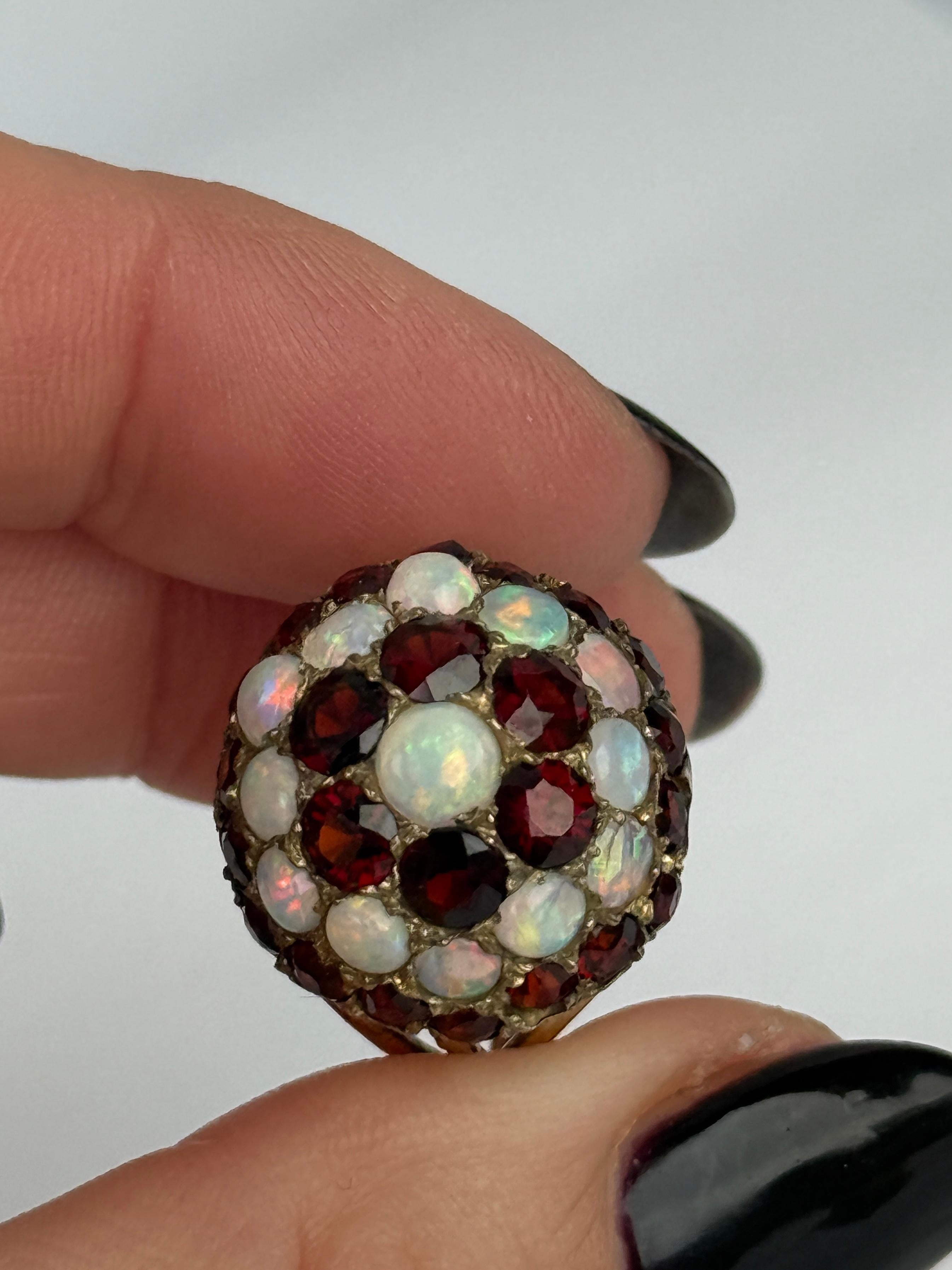 Questo anello di grande effetto contiene granati di 20 e 10 carati ciascuno. Tra i granati c'è un alone di opale con gli opali che misurano 15pt ciascuno e un opale più grande al centro che misura 35pt. Tutte le pietre sono inserite in griffe d'oro