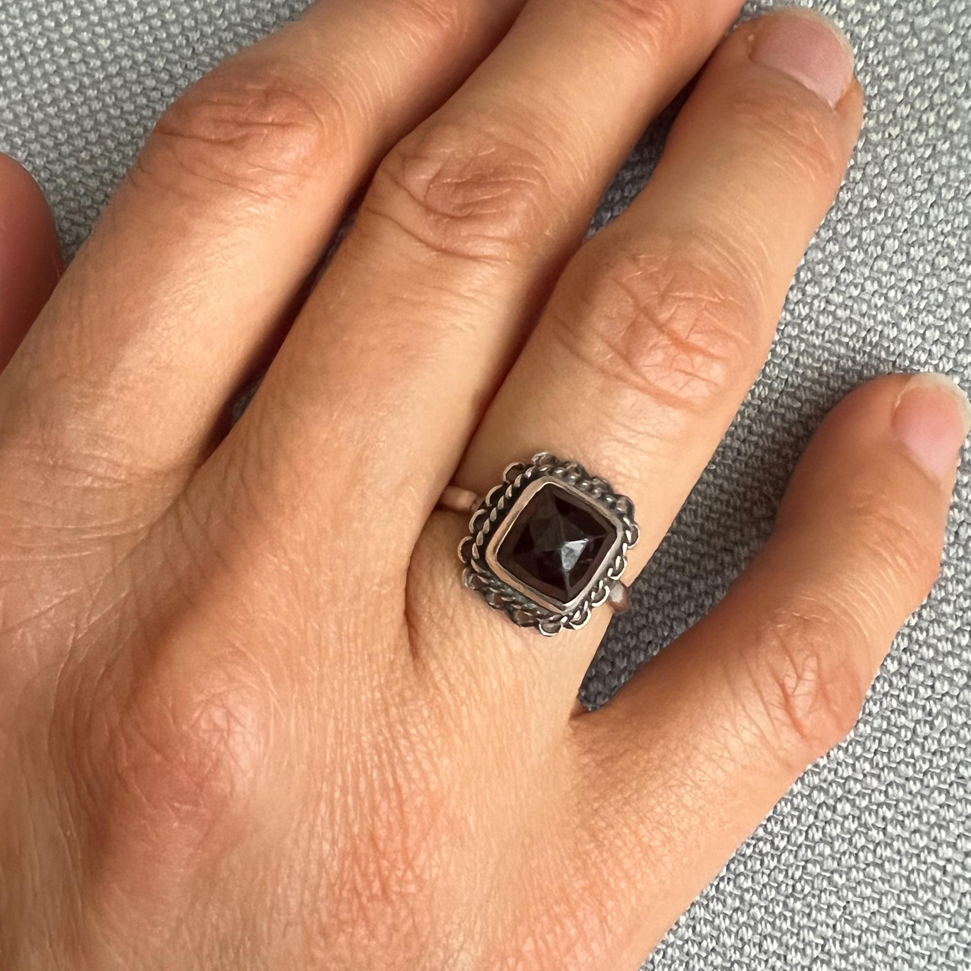 A preloved garnet ring made in silver. This lovely silver square shaped ring is set with a faceted garnet stone. The ring has a great design with one cute square garnet stone set in a silver openwork ornate border with rope motif. A piece to cherish