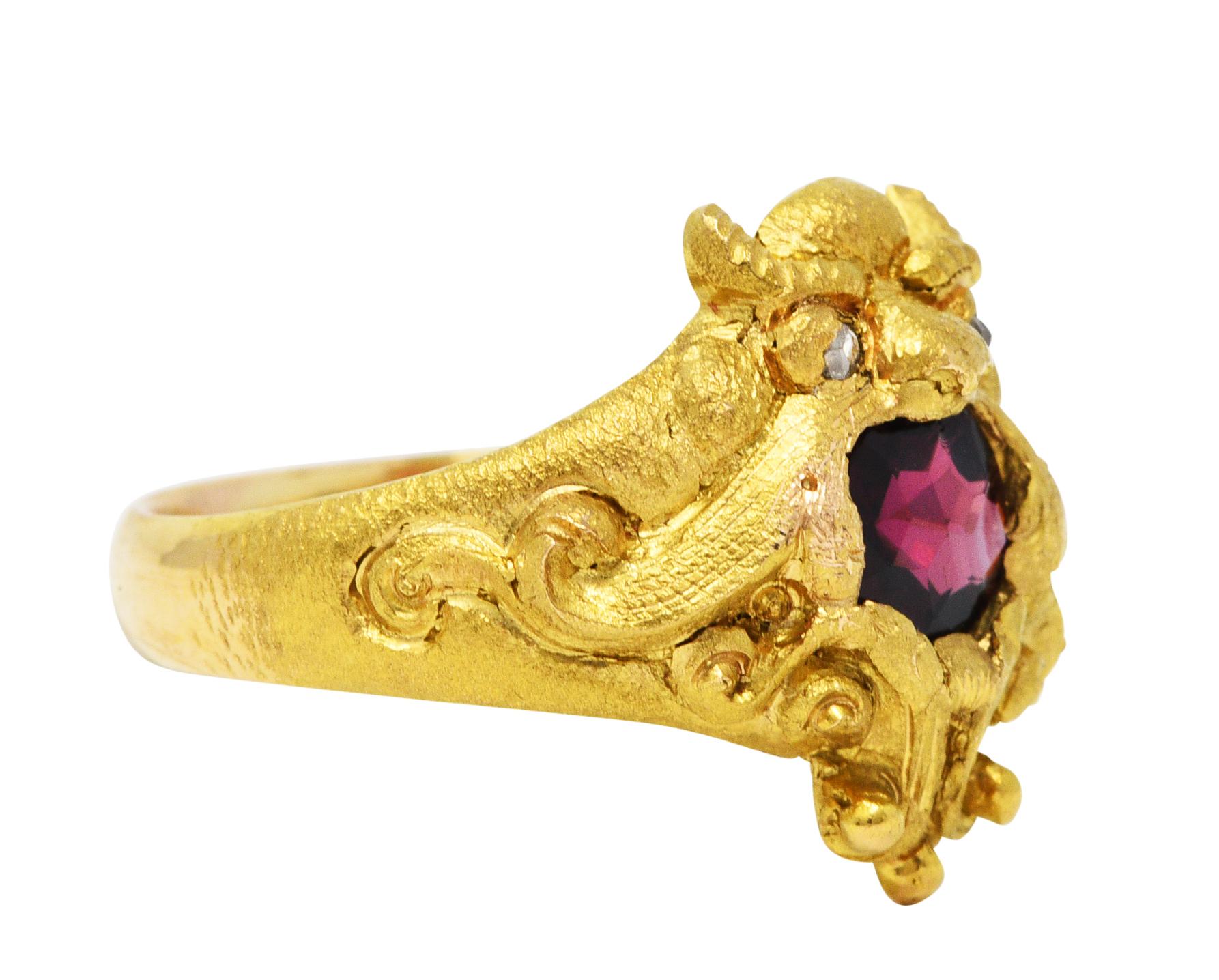 Band ring depicts a highly rendered gargoyle grotesque

Horned with scrolling whiplash and rose cut diamond eyes

Featuring a round cut garnet measuring approximately 5.5 mm and saturated red in color

Completed by a texturous matte gold