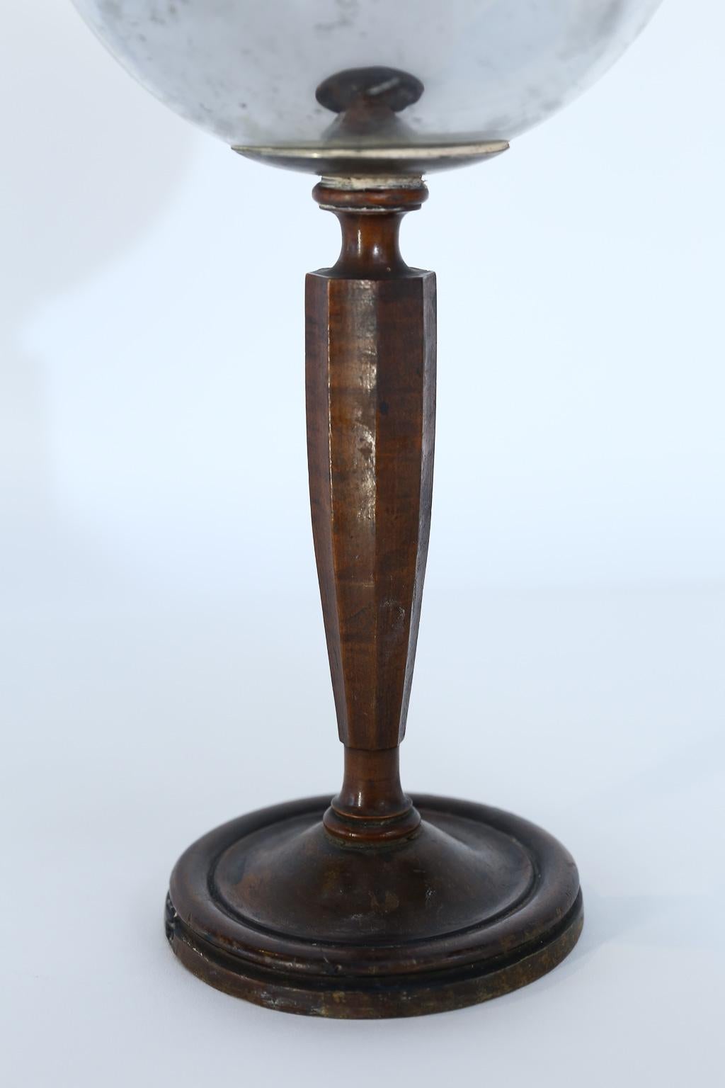 This vintage gazing ball on wood stand is sure to be a conversation piece. The ball is in good condition with no chips or cracks, yet it does show its age with some discoloration and silvering loss. Firmly attached to the wood base, the piece would