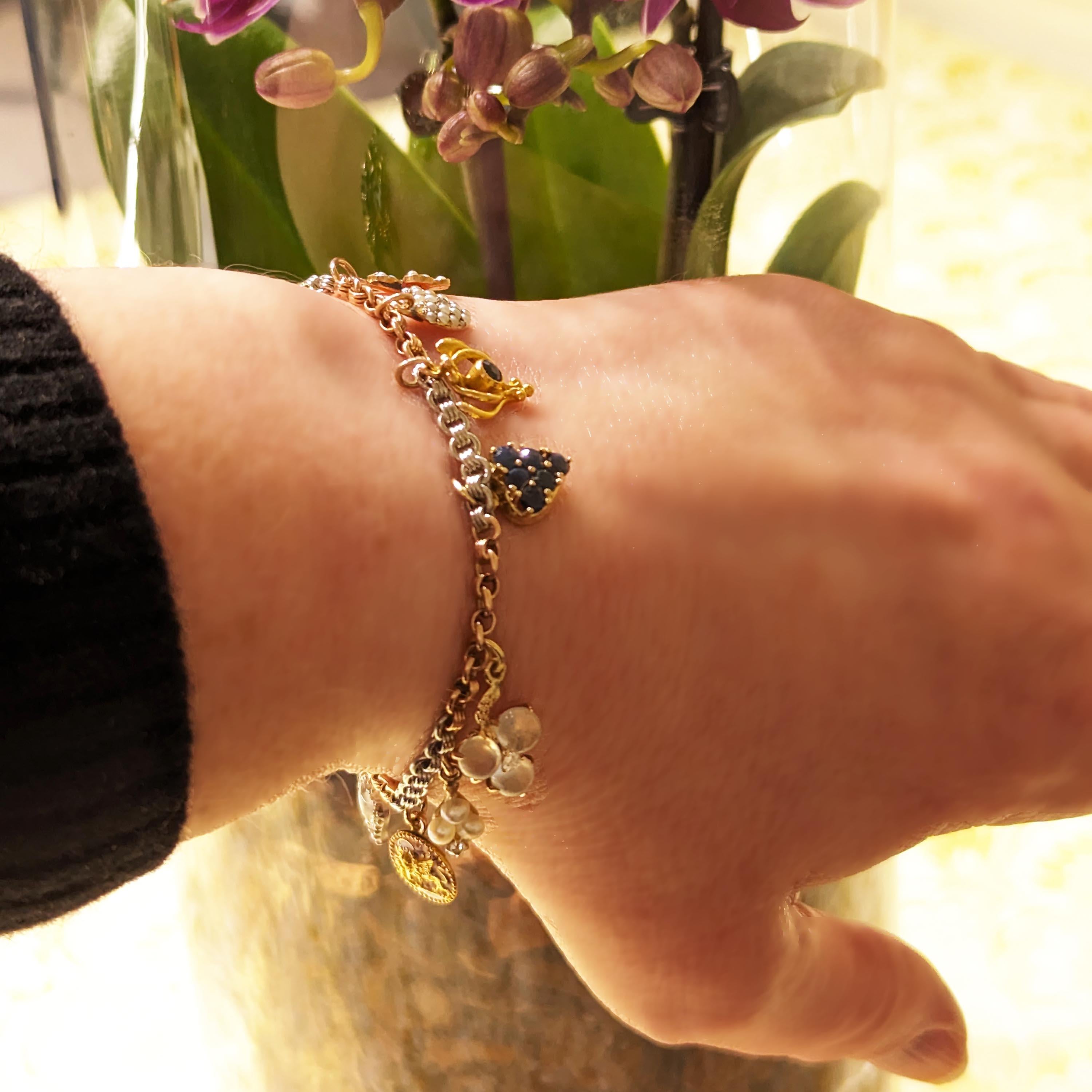 A vintage gemstone, enamel, gold and platinum charm bracelet, with charms from left to right featuring: a gold foliate design on a dark blue enamel background, in gold, with a hair locket in the back; a gold crown, with enamel depicting blue, green