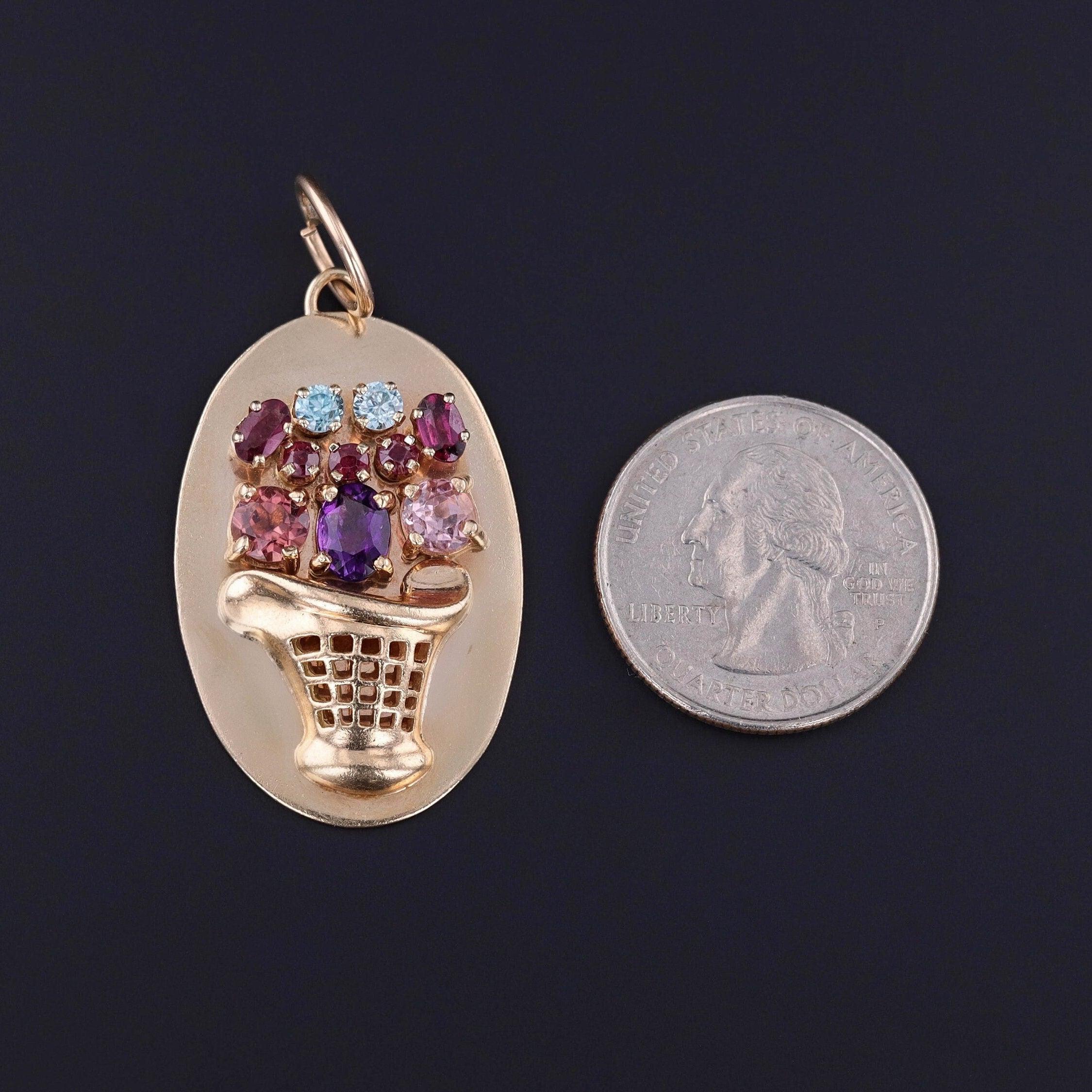 Questo ciondolo in oro 14k della metà del secolo scorso (1950-1960 circa) presenta un cesto di fiori di gemme con zirconi blu, granati, ametiste, rubini e tormaline. Sul retro sono incise le iniziali FHM.

Il pezzo vintage misura 1,9 pollici