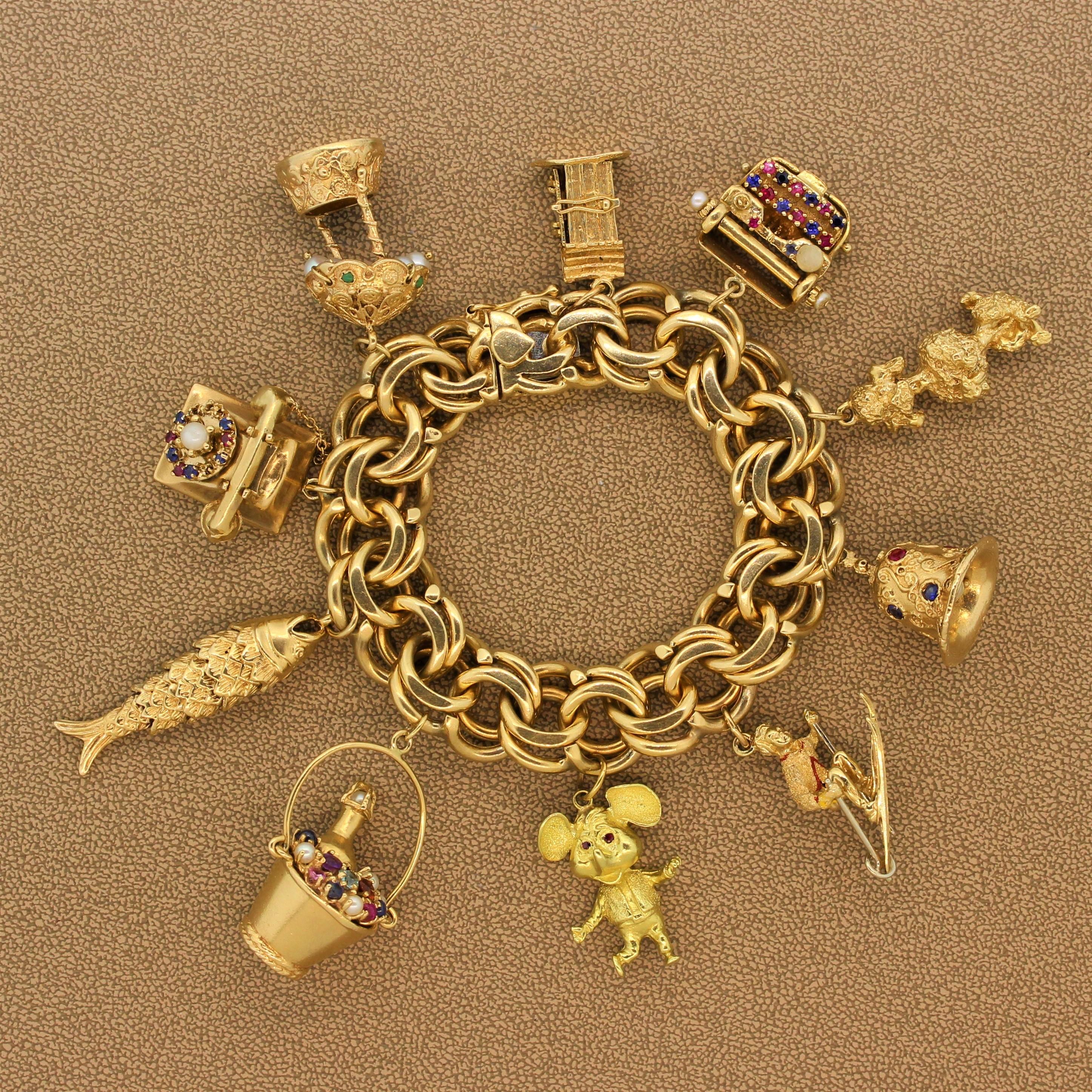 Charmed! This estate charm bracelet made of 14K yellow gold linked hoops has ten uniquely fun charms. A cabin, typewriter, poodle, bell, skier, cartoon mouse, champagne, fish, telephone and canopy with multi-color gemstones and pearls make this