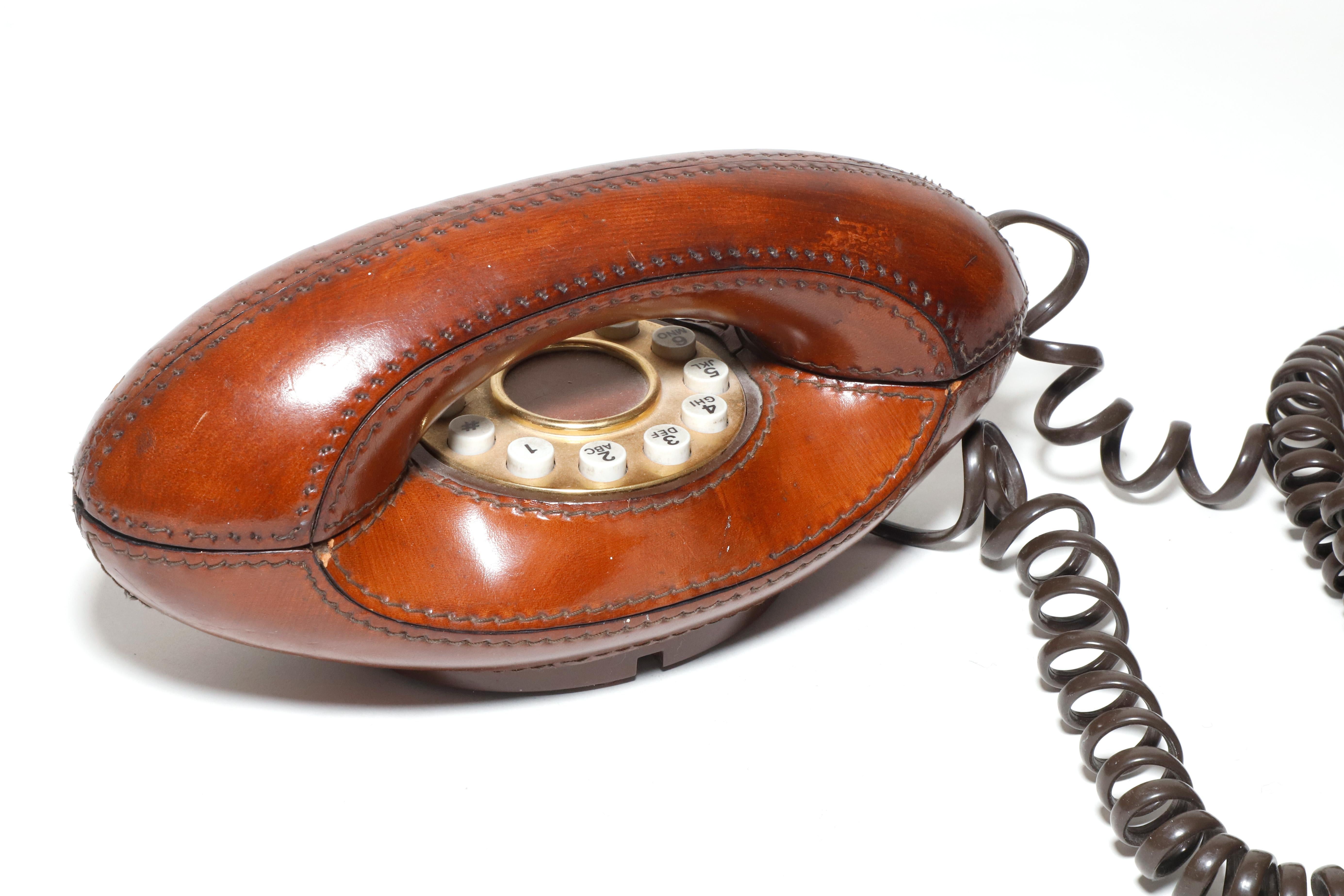 Wunderschönes, mit braunem Leder bezogenes Vintage-Telefon mit aufwendigen Nähten und Messingplatte um die Drucktasten. Hergestellt von Genie und entworfen in den späten 1970er Jahren in den USA. Dieses Modell erfreute sich zu seiner Zeit großer